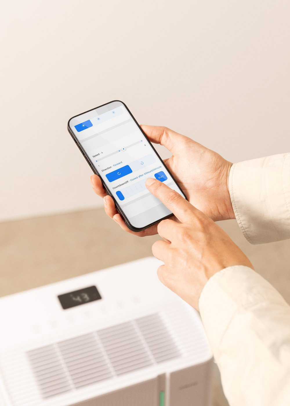 Una mano sostiene un teléfono inteligente, mostrando la interfaz de una aplicación. Un purificador de aire blanco está en el fondo, con el número 43.