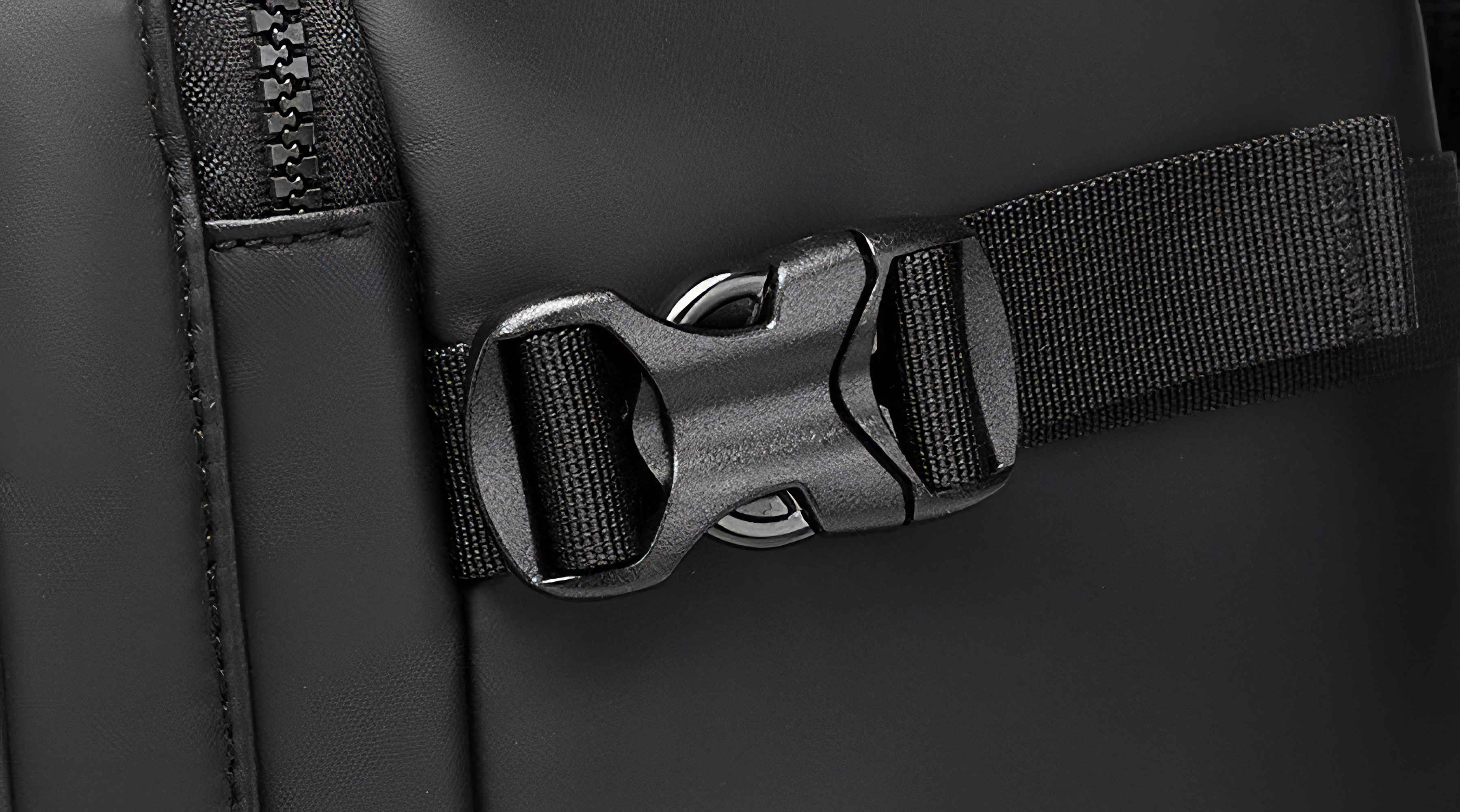 Nahaufnahme eines schwarzen Rucksackdetails. Eine schwarze Kunststoffschnalle befindet sich an einem schwarzen Riemen. Ein Reißverschluss befindet sich links.