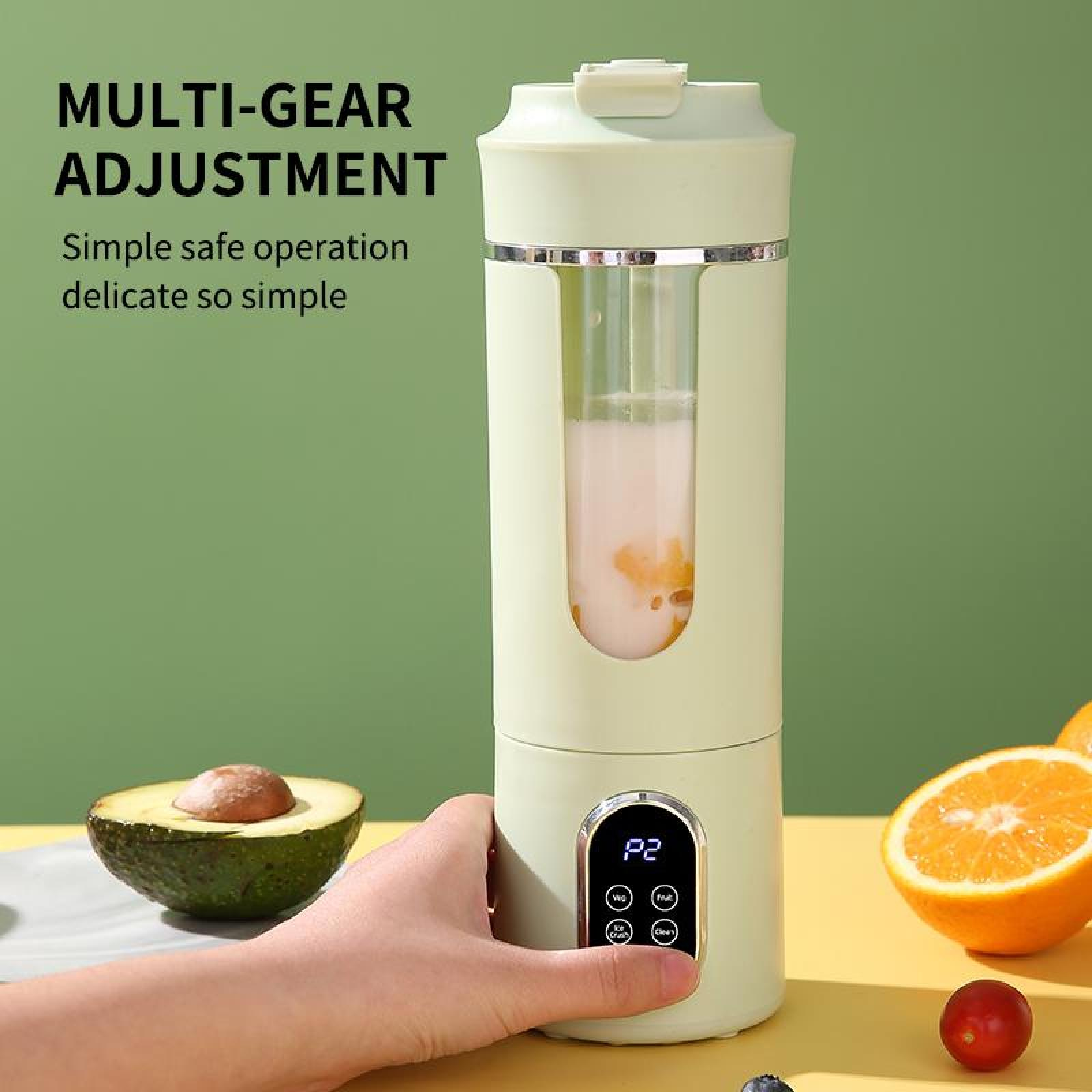 Eine Hand bedient einen grünen Mixer. Eine Avocado, Orange und kleine Frucht liegen auf gelber Oberfläche. Grüner Hintergrund.