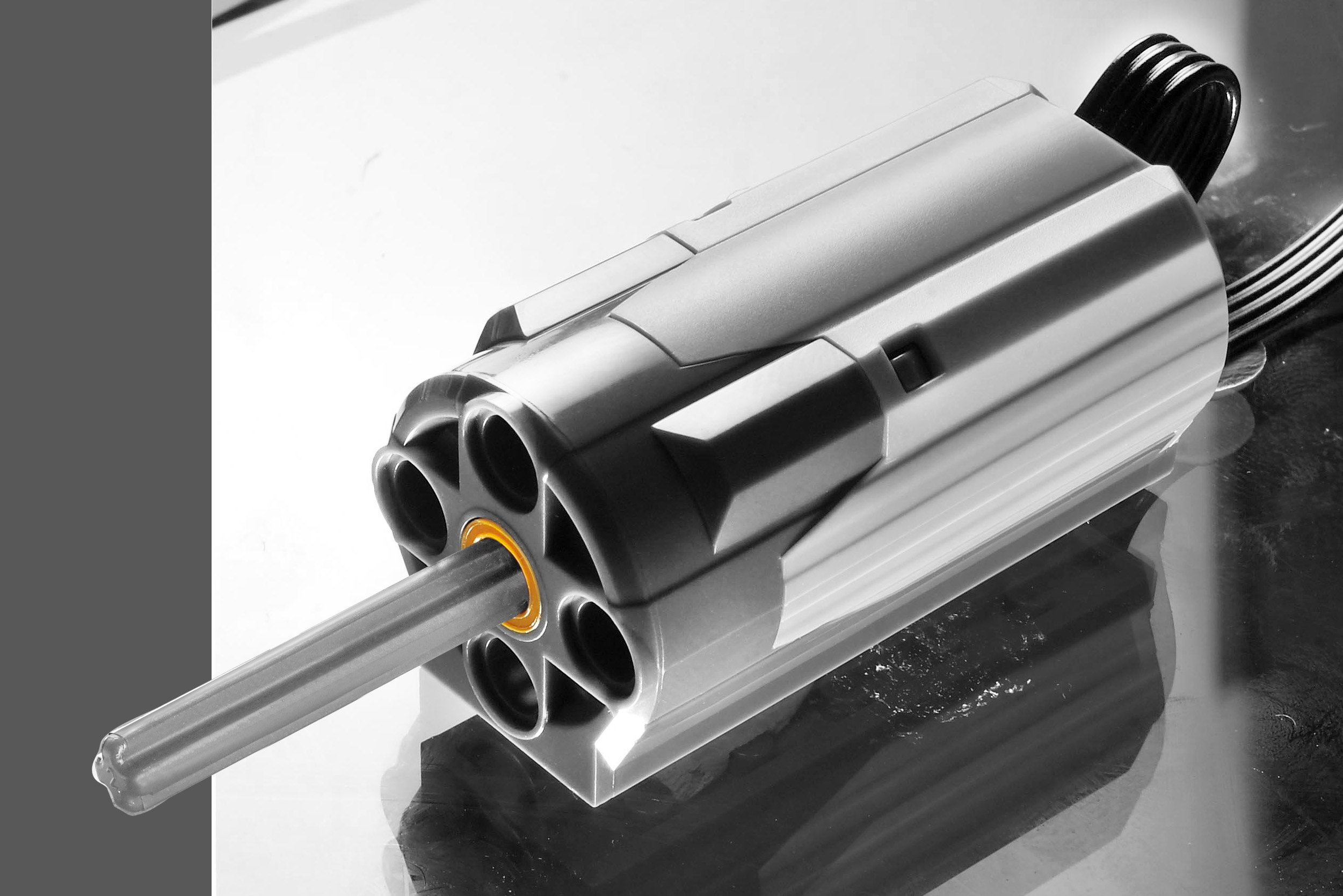 Obraz w skali szarości elementu mechanicznego. Ma cylindryczny kształt z wieloma otworami. Wystaje z niego pręt.