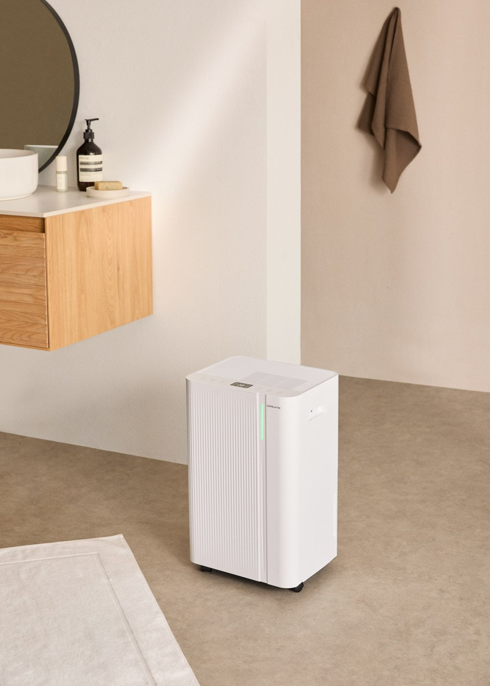Un purificador de aire blanco está en un baño. Una toalla cuelga en la pared. Un lavabo y espejo están a la izquierda.