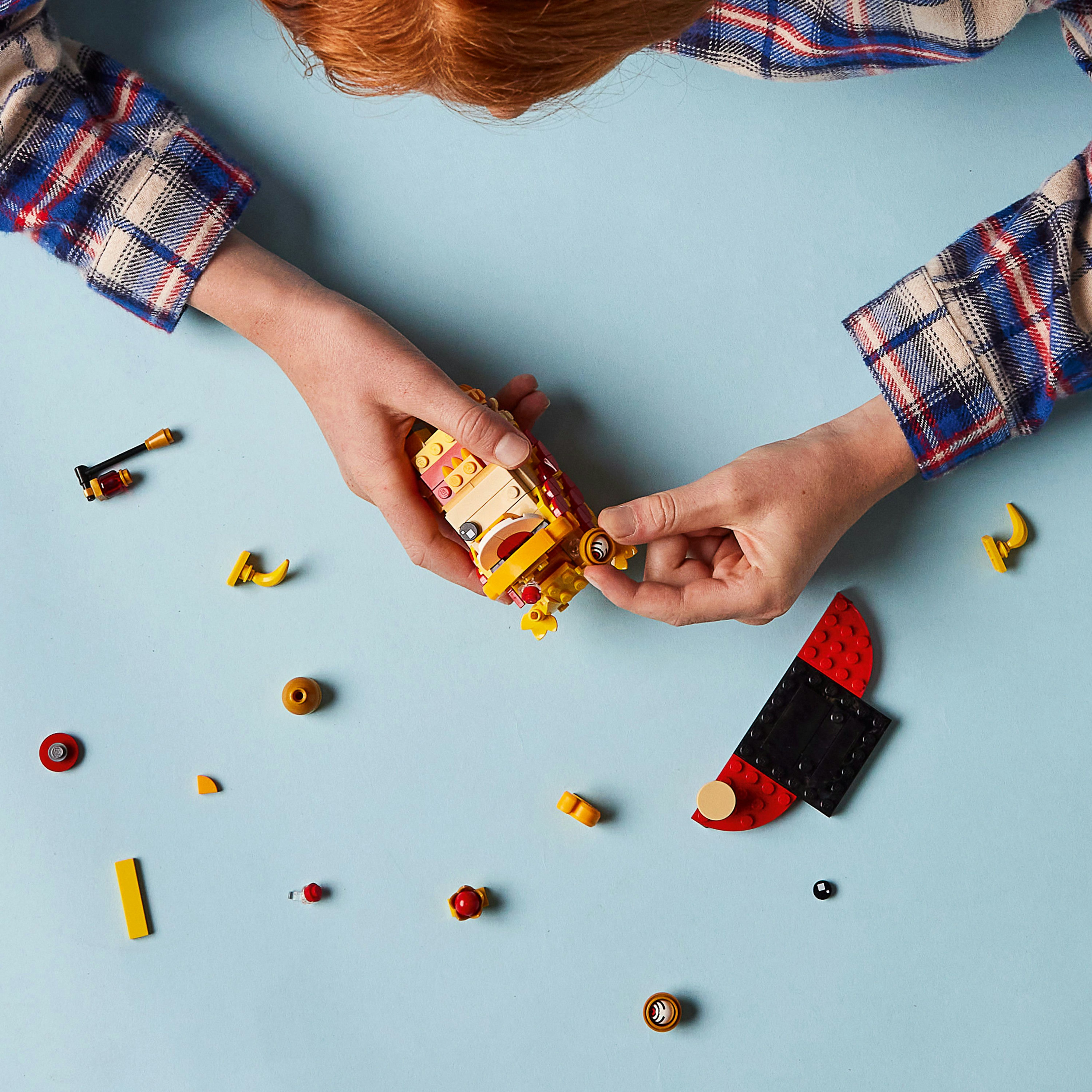 Mani che assemblano un'auto Lego su una superficie blu. Diversi pezzi Lego sparsi, tra cui ruote e parti della carrozzeria.