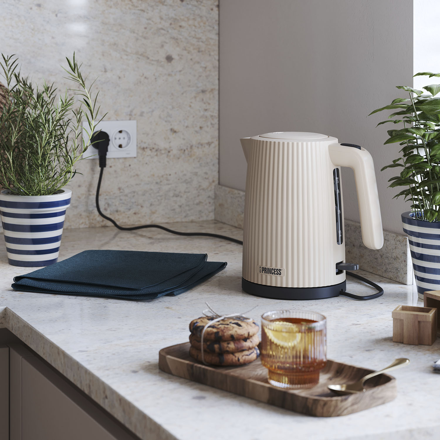 Beżowy czajnik Princess, filiżanka herbaty z cytryną, ciastka i rośliny na blacie. Niebieskie doniczki w paski z roślinami. Gniazdko elektryczne.