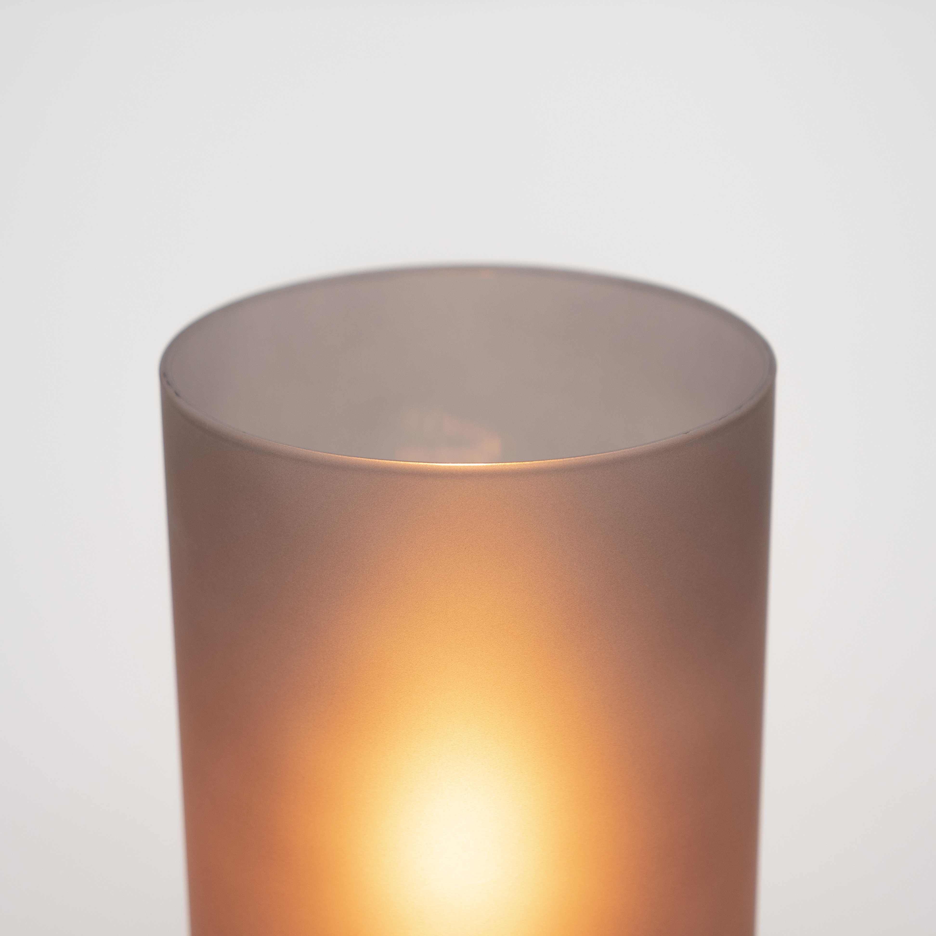 Eine zylindrische Lampe mit warmer Lichtquelle, sichtbar durch den durchscheinenden Körper, vor weißem Hintergrund.