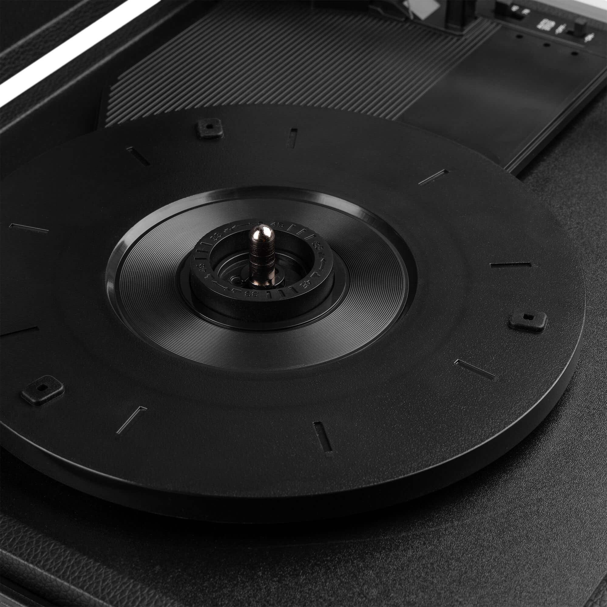 Close-up of a black record player with a rotating disc. The disc has numbers, a metal spindle, and is surrounded by a black base.
