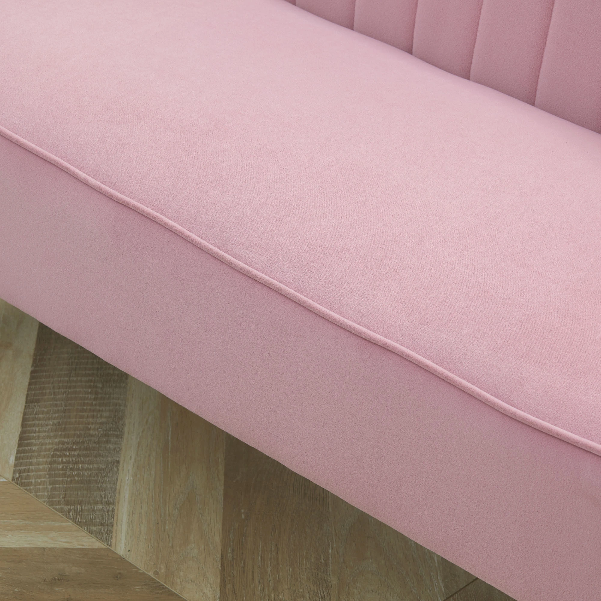 Nahaufnahme eines rosa Sofas mit Holzboden. Das Sofa besteht aus Samt und hat eine Naht. Der Boden ist hellbraun.