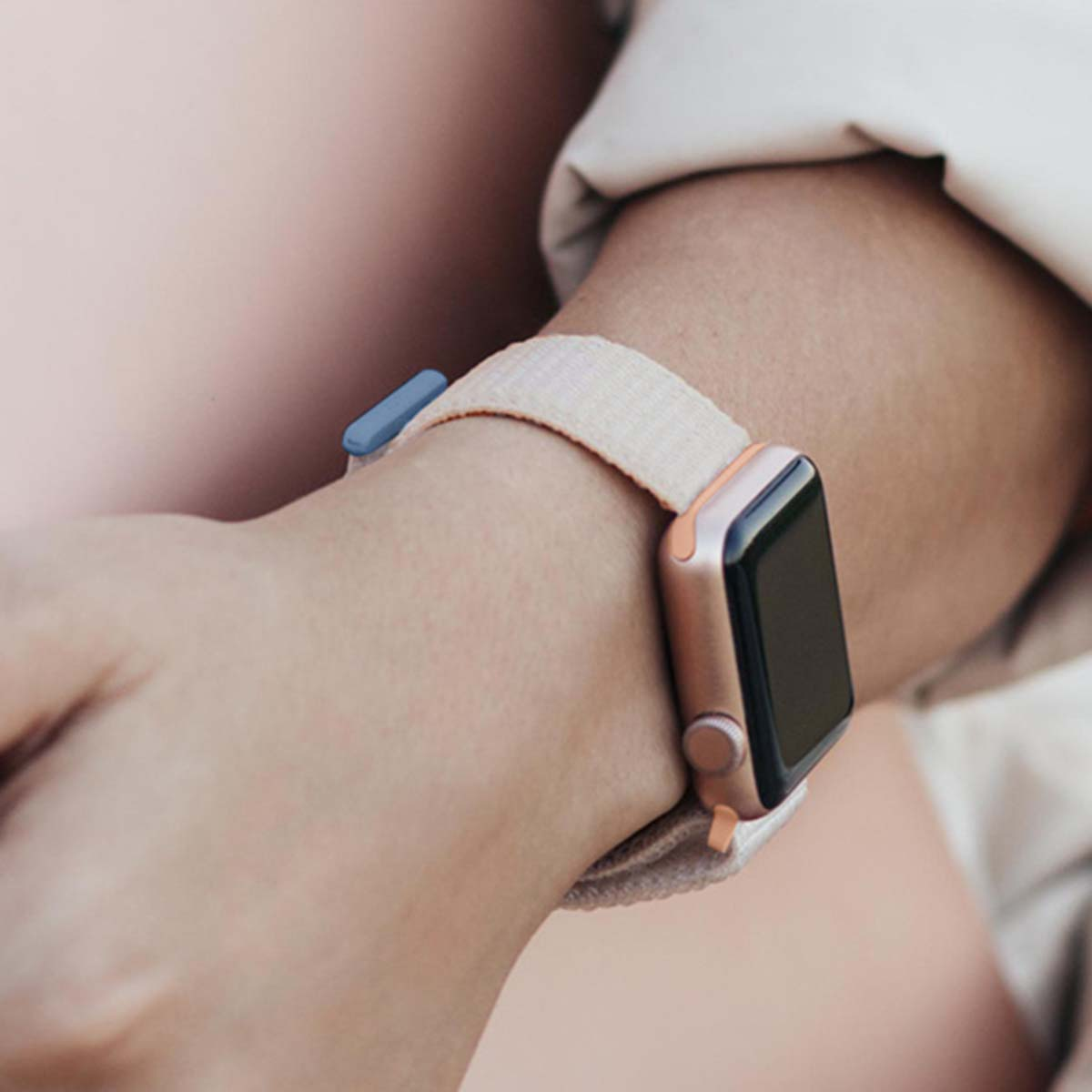Primo piano di un polso con un Apple Watch con cinturino rosa chiaro. Il quadrante dell'orologio è nero. Lo sfondo è sfocato.