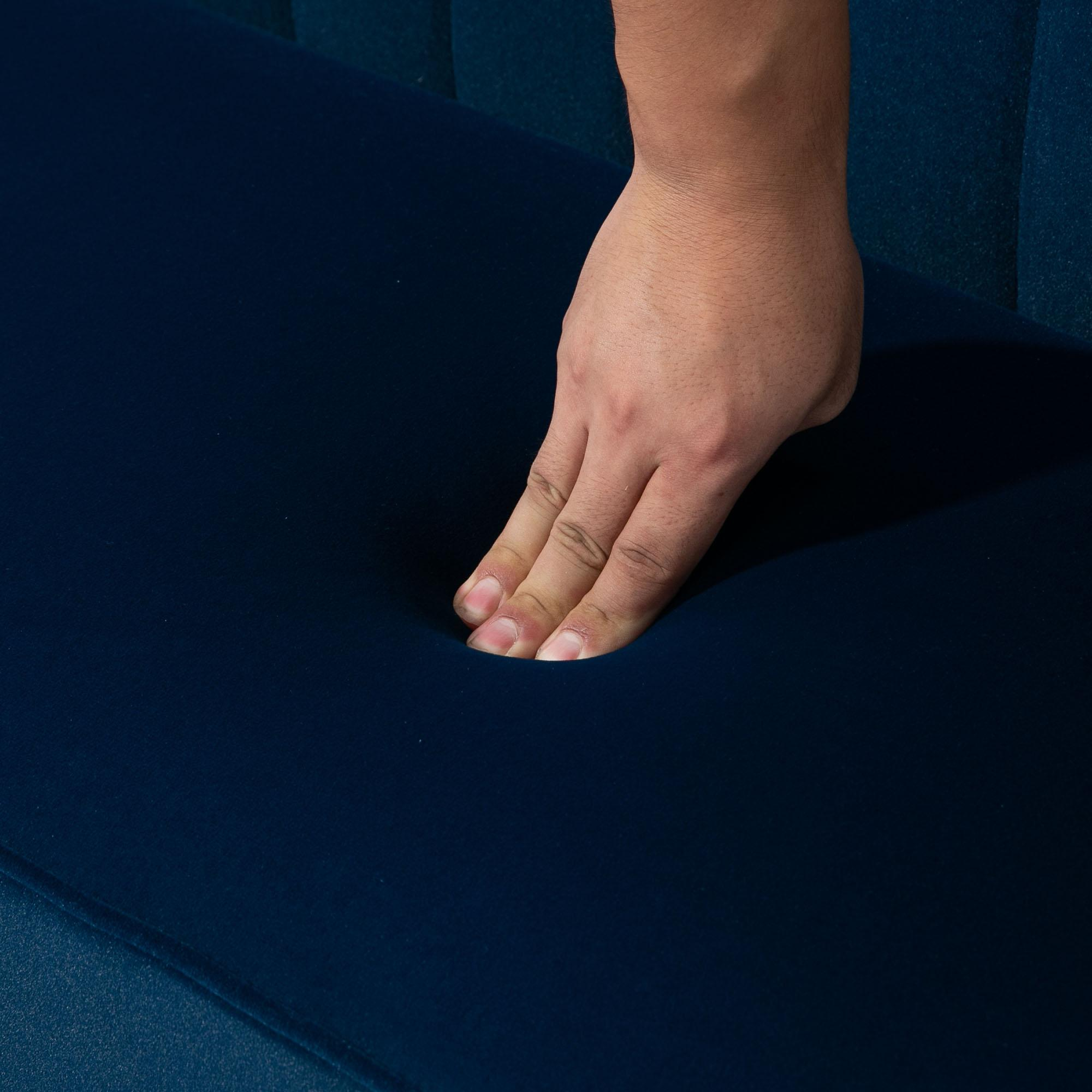 Eine Hand drückt auf eine dunkelblaue, gepolsterte Oberfläche. Die Hand ist teilweise sichtbar. Die Oberfläche hat eine Struktur.