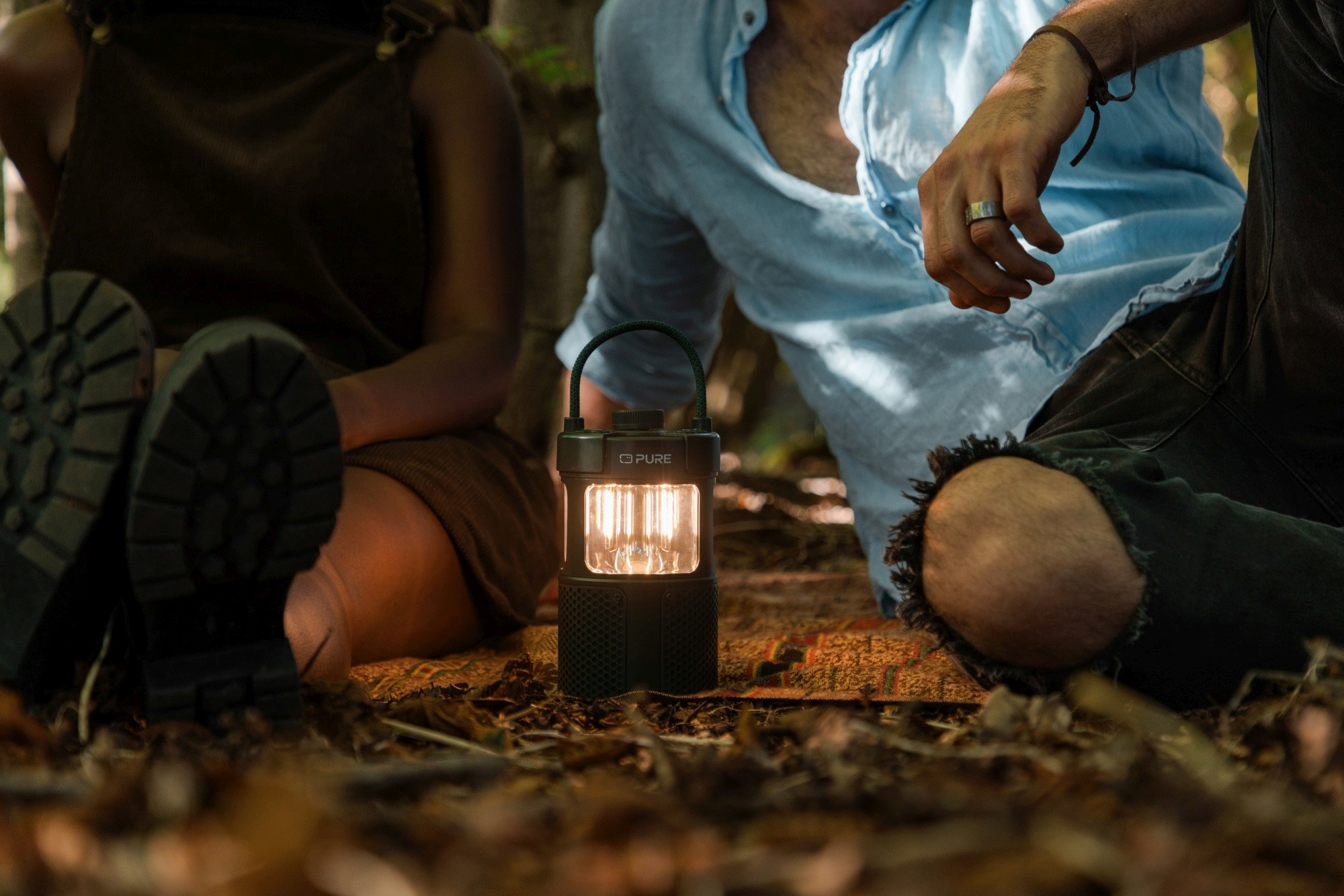 Dwie osoby siedzą w pobliżu świecącej latarni. Jedna ma na sobie niebieski strój, druga brązowy. Scena rozgrywa się na zewnątrz. Liście pokrywają ziemię.