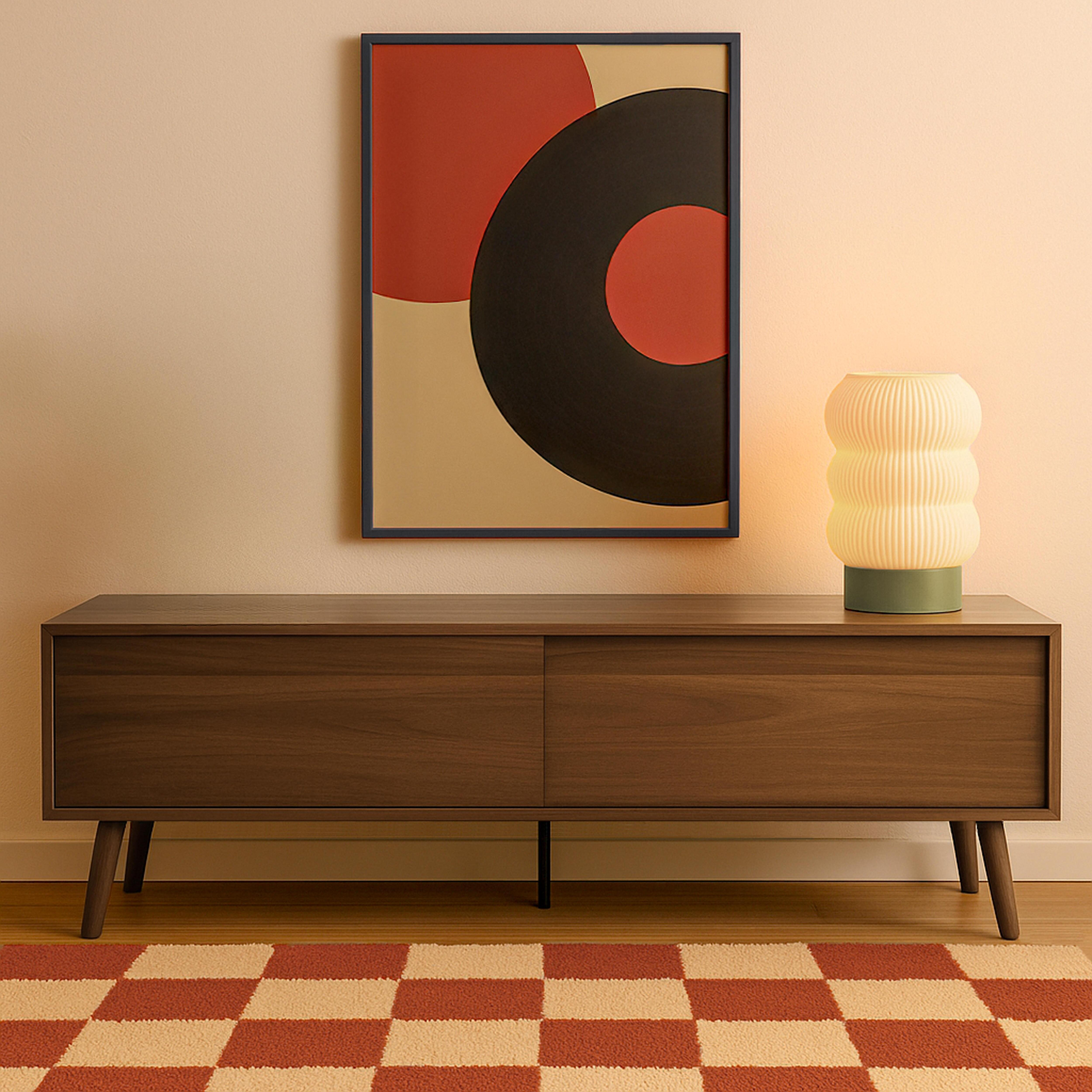 Ein Holzschrank mit Lampe und gerahmtem Kunstwerk steht auf einem karierten Teppich. Eine Wand ist dahinter.