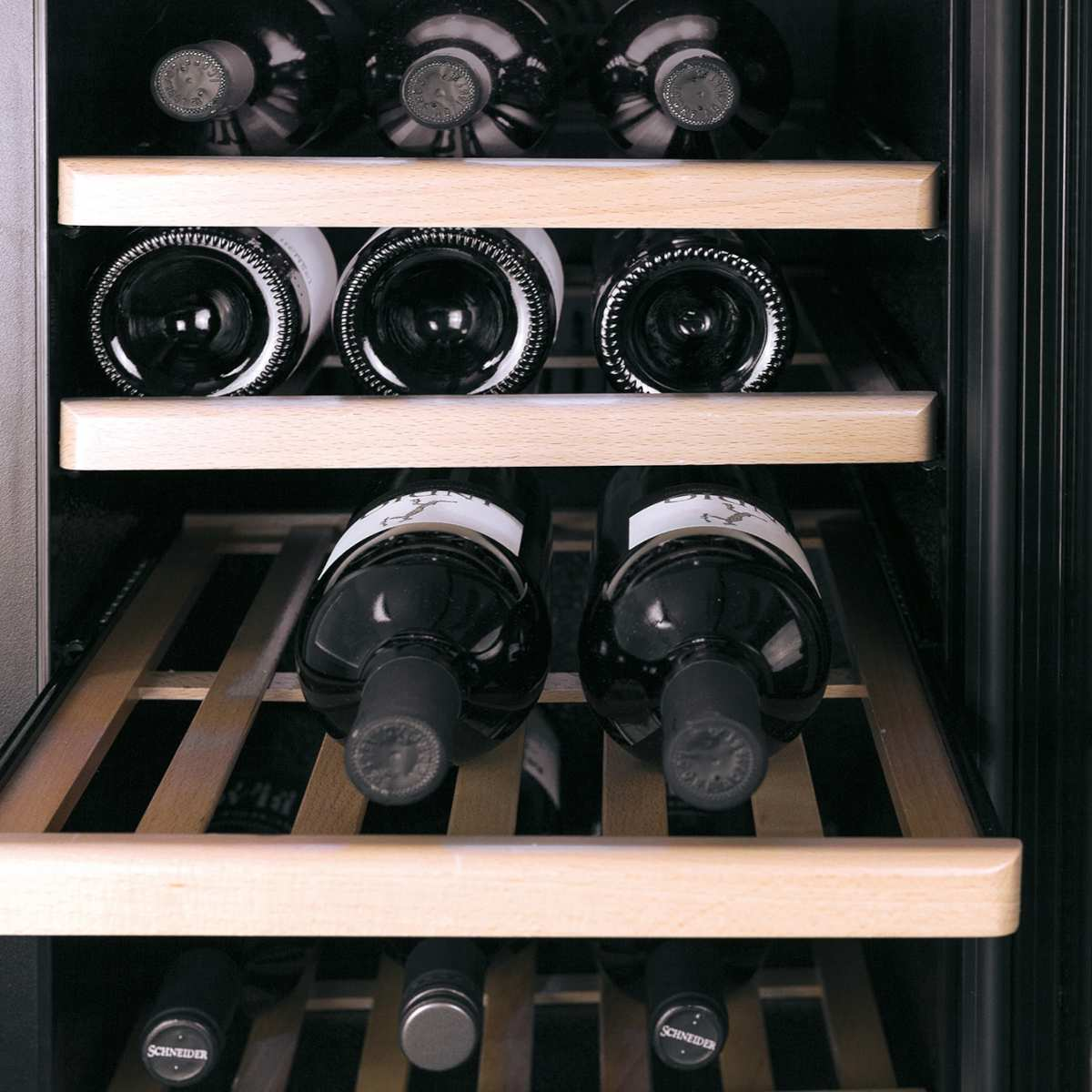 Wein Flaschen in einem Kühlschrank. Regale halten die Flaschen. Die Flaschen sind dunkel mit hellen Etiketten. Der Kühlschrank ist schwarz und Holz.