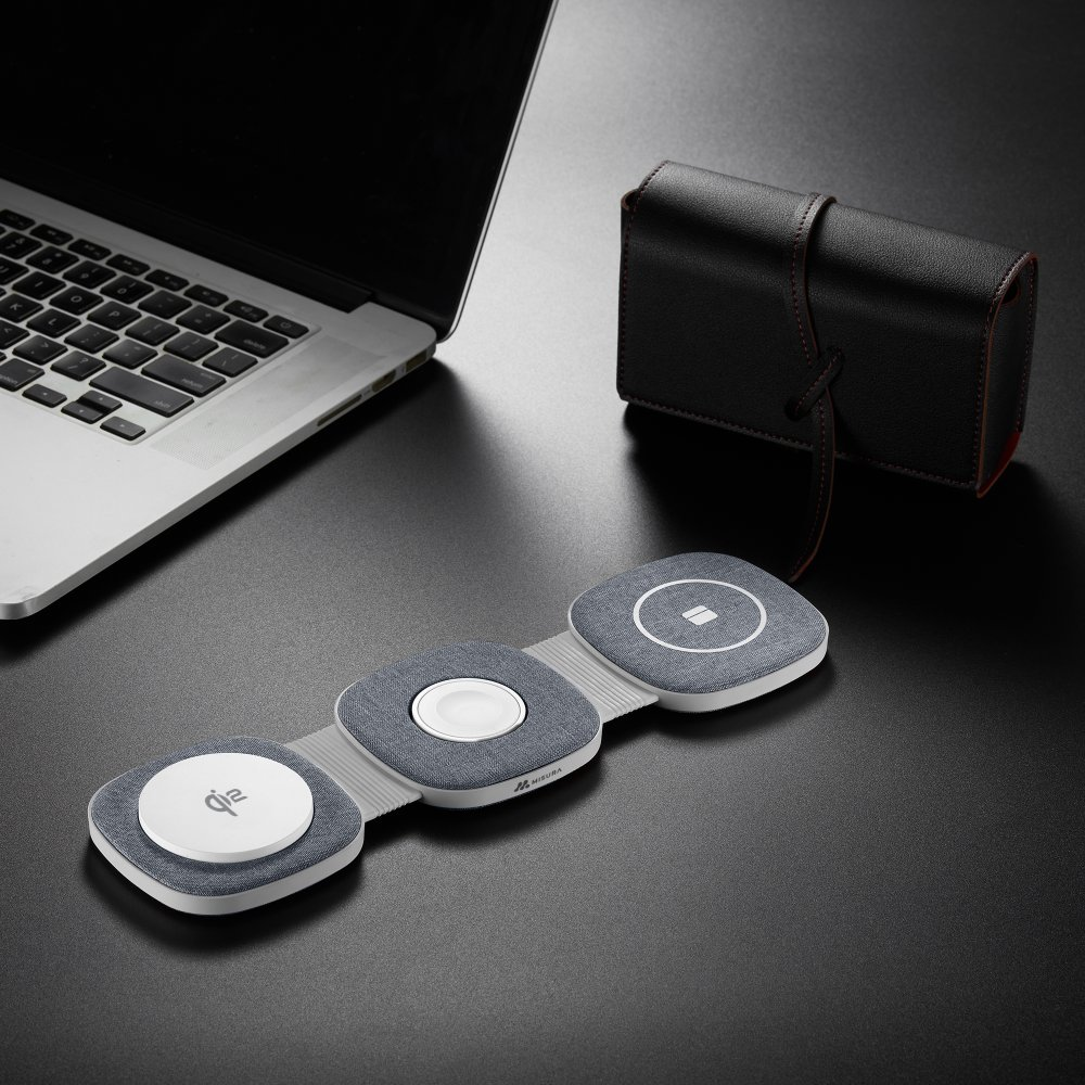 Bezprzewodowa podkładka ładująca z trzema punktami ładowania, laptop i czarne skórzane etui na czarnej powierzchni.