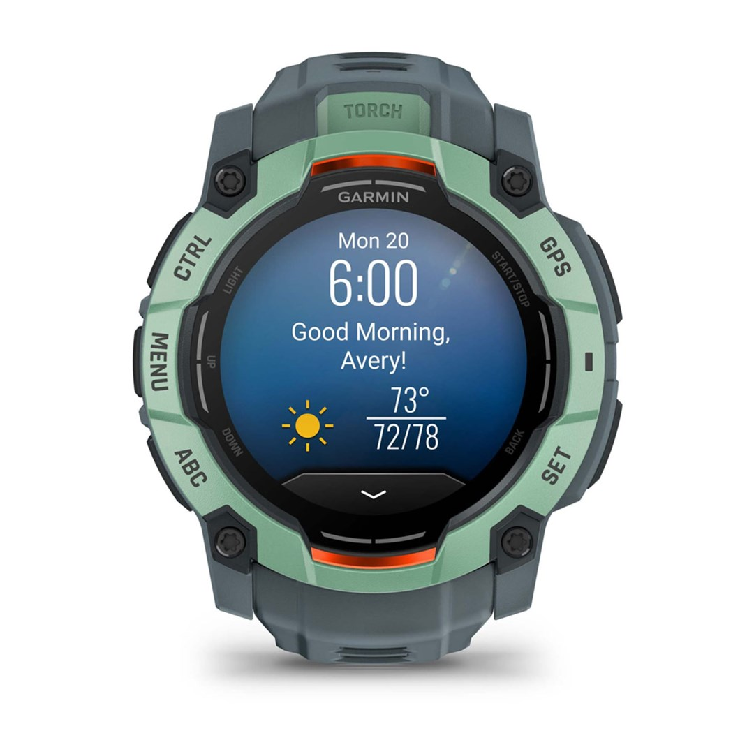 Smartwatch Garmin wyświetla 'Dzień dobry, Avery!' z informacjami o pogodzie. Ma zielono-szarą obudowę z przyciskami sterowania i GPS.