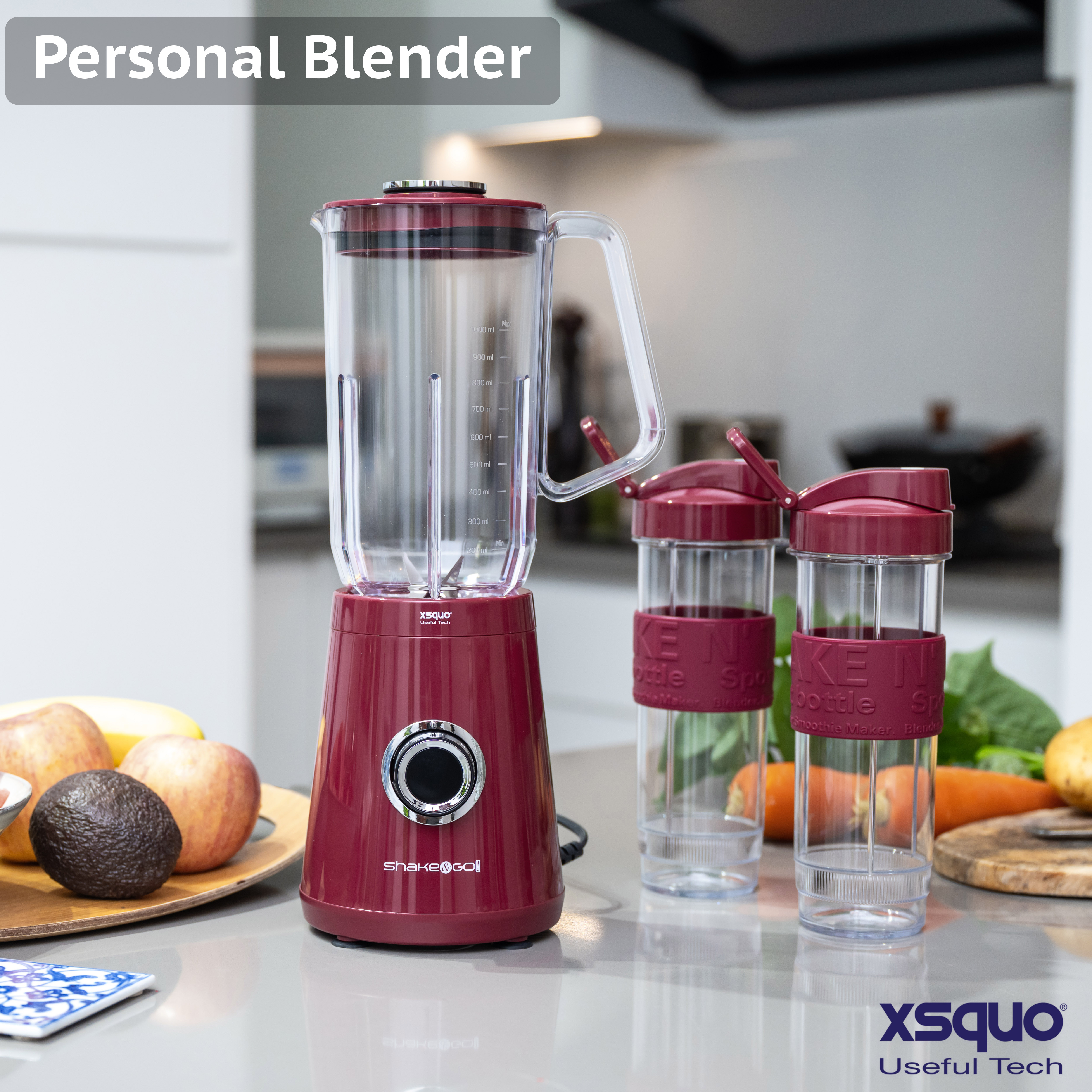 Una batidora personal roja con dos botellas. Hay frutas a la izquierda. La batidora dice Shake&Go! y Xsquo Useful Tech.