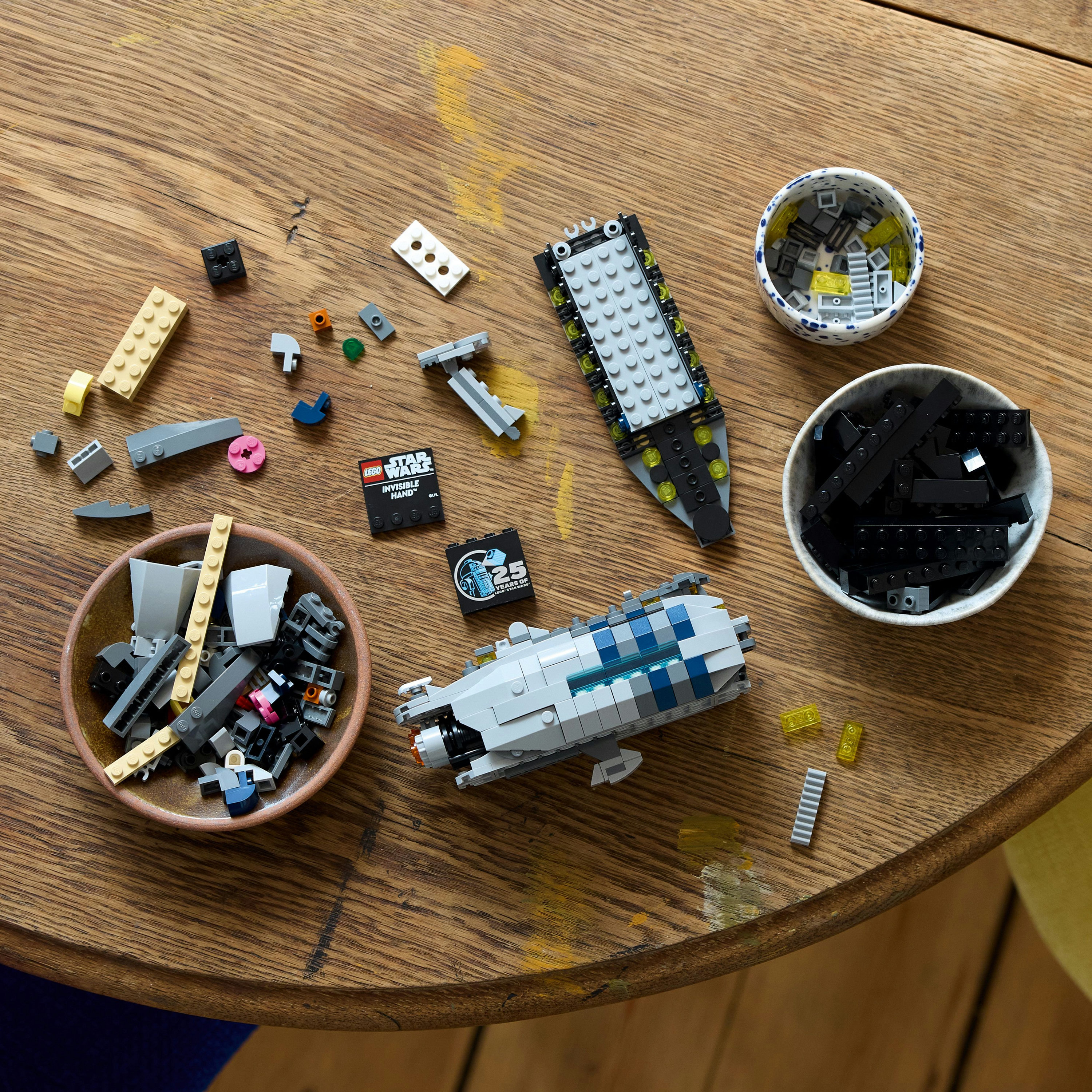 Zestaw Lego na drewnianym stole. Widoczne są części i dwa złożone statki. Różne elementy są w miskach.