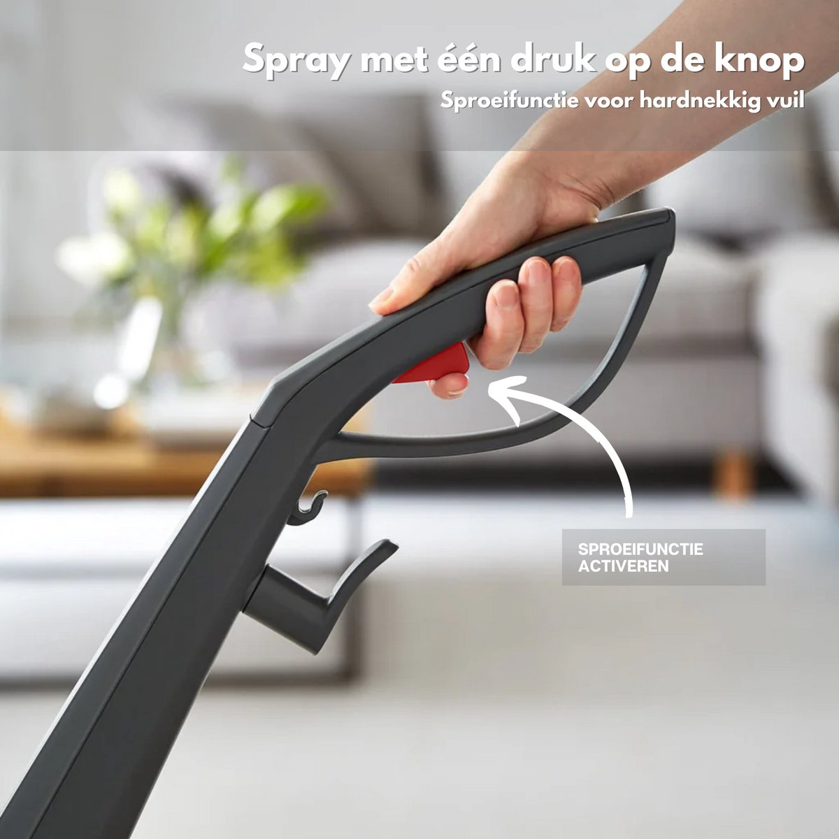 A hand presses a red button on a dark gray handle. A white arrow points to a button. The background is a blurry living room.