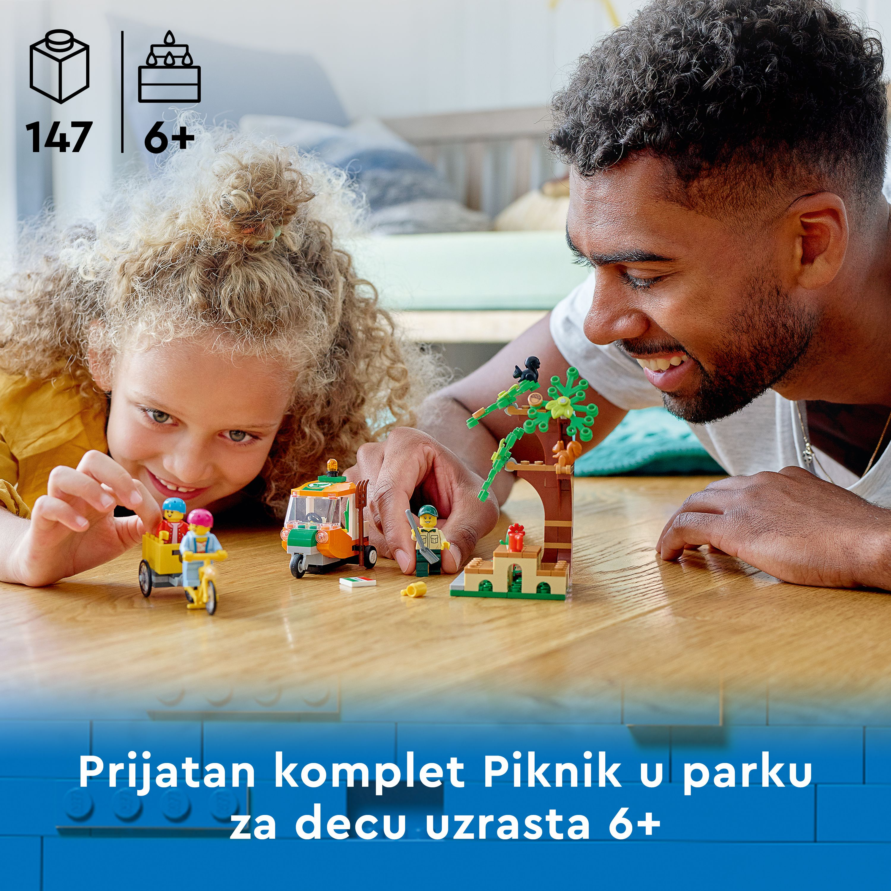 Bir baba ve çocuğu Lego piknik setleriyle oynuyor. Setler arasında bir yiyecek kamyonu, bir park sahnesi ve figürler bulunur.