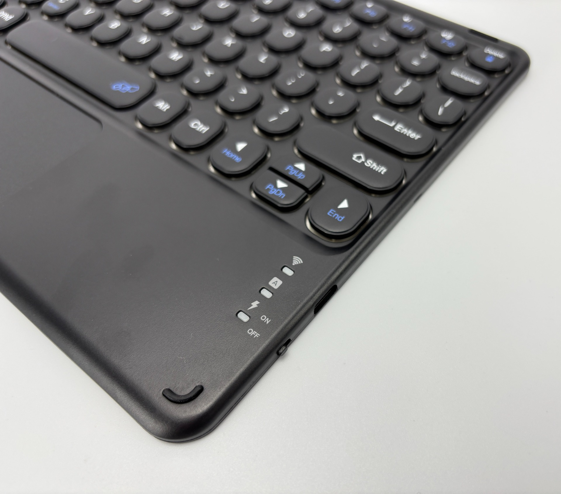 Black keyboard with round keys, including function keys, indicators on the side, and a touchpad. White background.