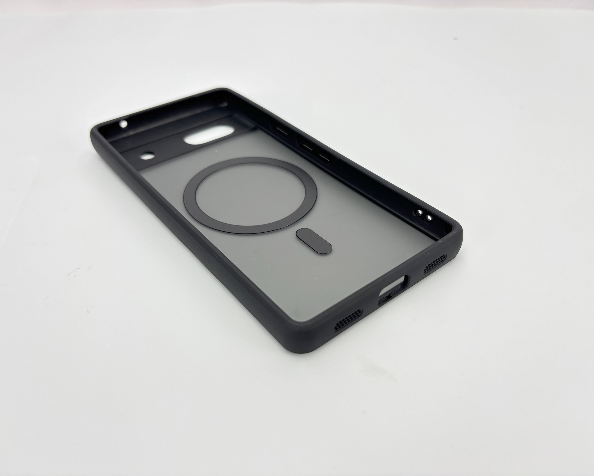 Custodia nera per telefono con anello magnetico e piccolo rettangolo. Su una superficie bianca. La custodia è vuota.