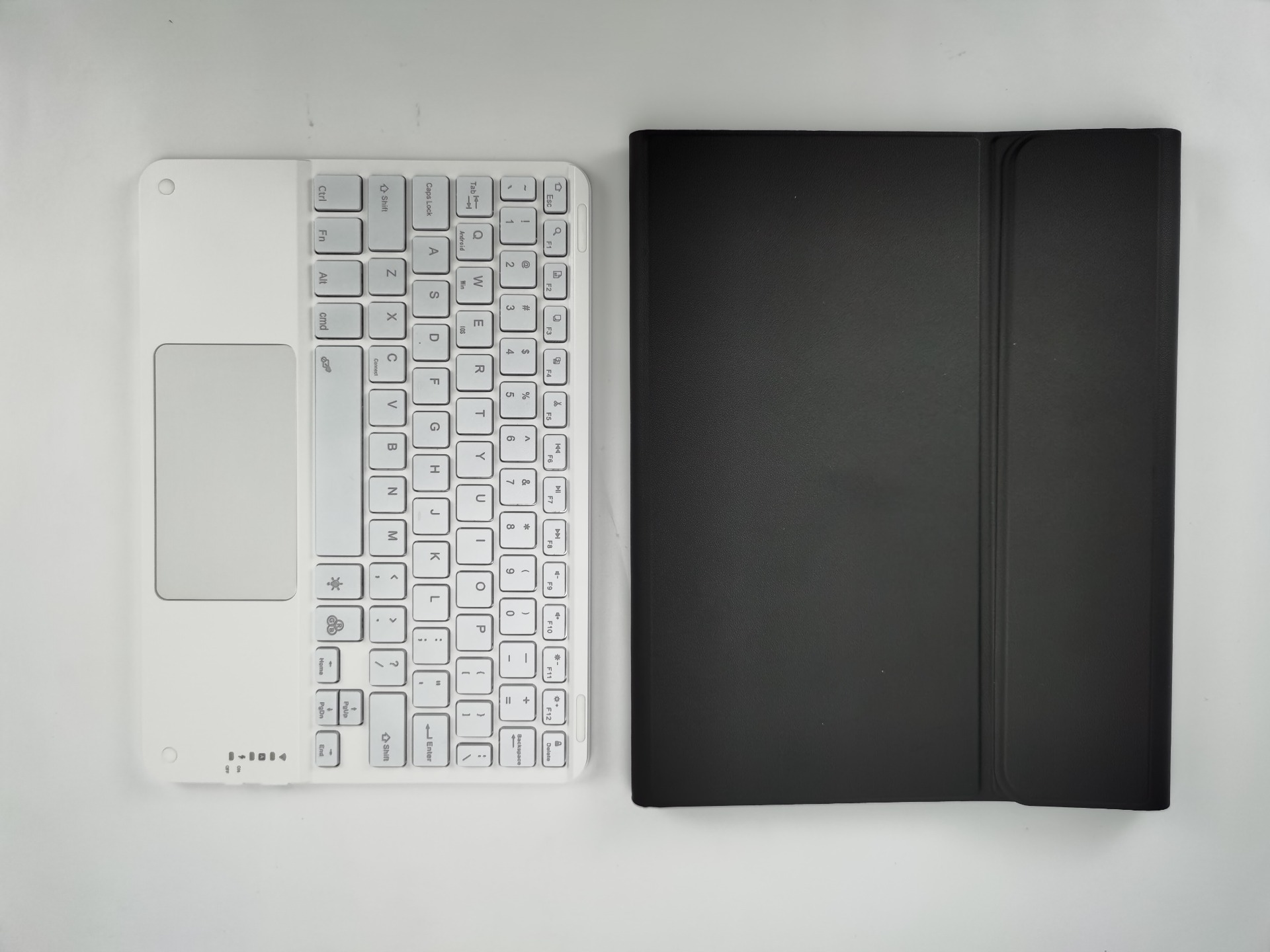 Eine weiße Tastatur und eine schwarze Tablethülle liegen auf einer weißen Oberfläche. Die Tastatur hat Tasten und ein Touchpad.