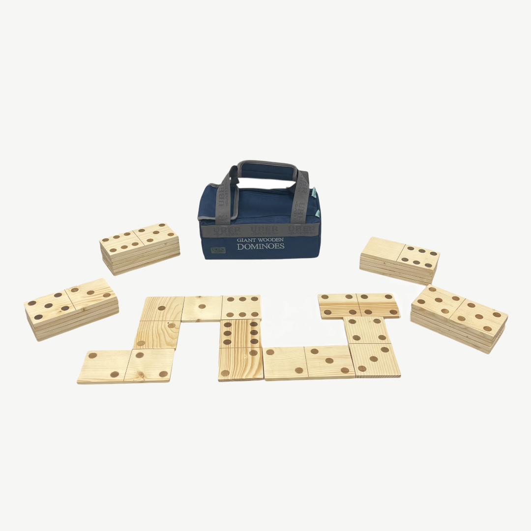 Ein Satz riesiger Holzdominos, angeordnet auf einer weißen Oberfläche, mit einer blauen Tasche im Hintergrund. Die Dominosteine sind helles Holz.