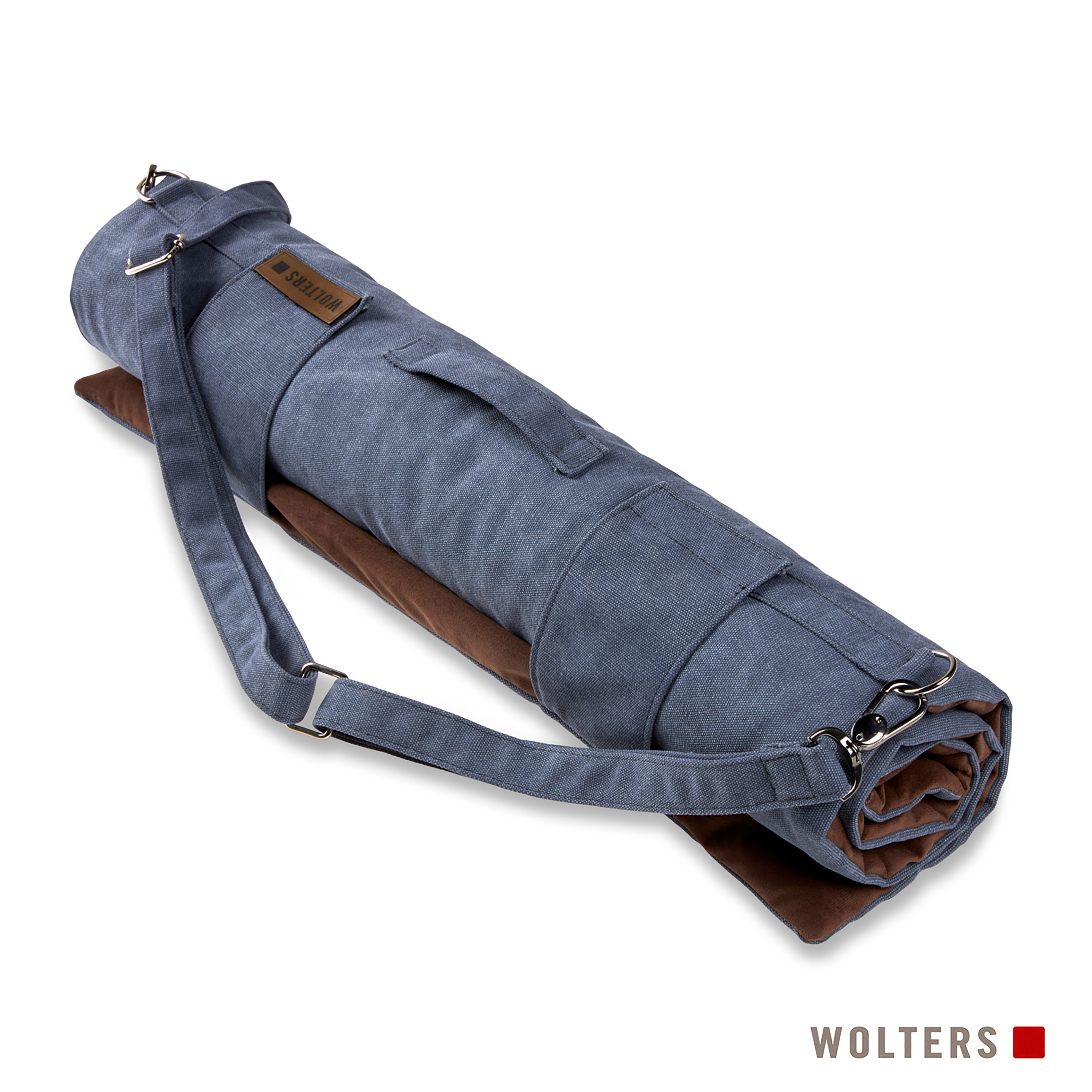Gerollte graue Matte in einer blauen Tasche mit Schultergurt, auf einem braunen Kissen, mit Wolters-Logo.