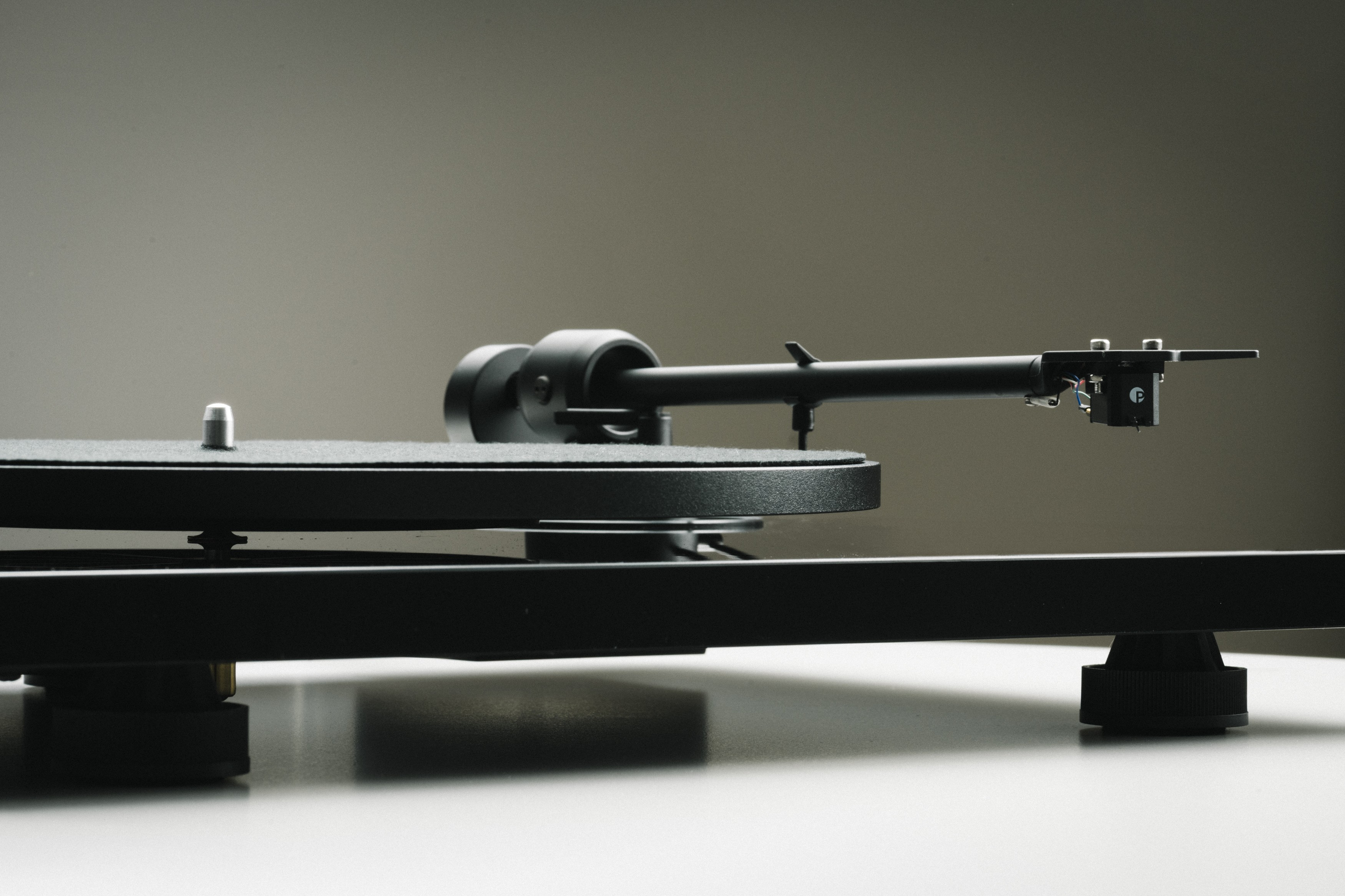 Czarny gramofon z ramieniem na białej powierzchni. Szare tło. Widok z bliska.