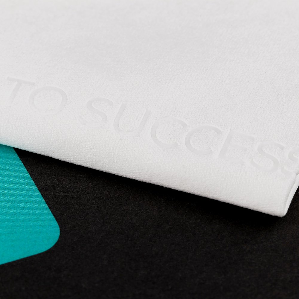 Tela blanca con texto en relieve 'TO SUCCESS' sobre fondo negro y verde azulado. La tela está doblada e iluminada desde arriba.