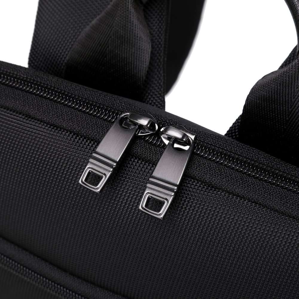 Primo piano di una borsa nera con due cerniere metalliche chiuse. Lo sfondo è una superficie bianca.