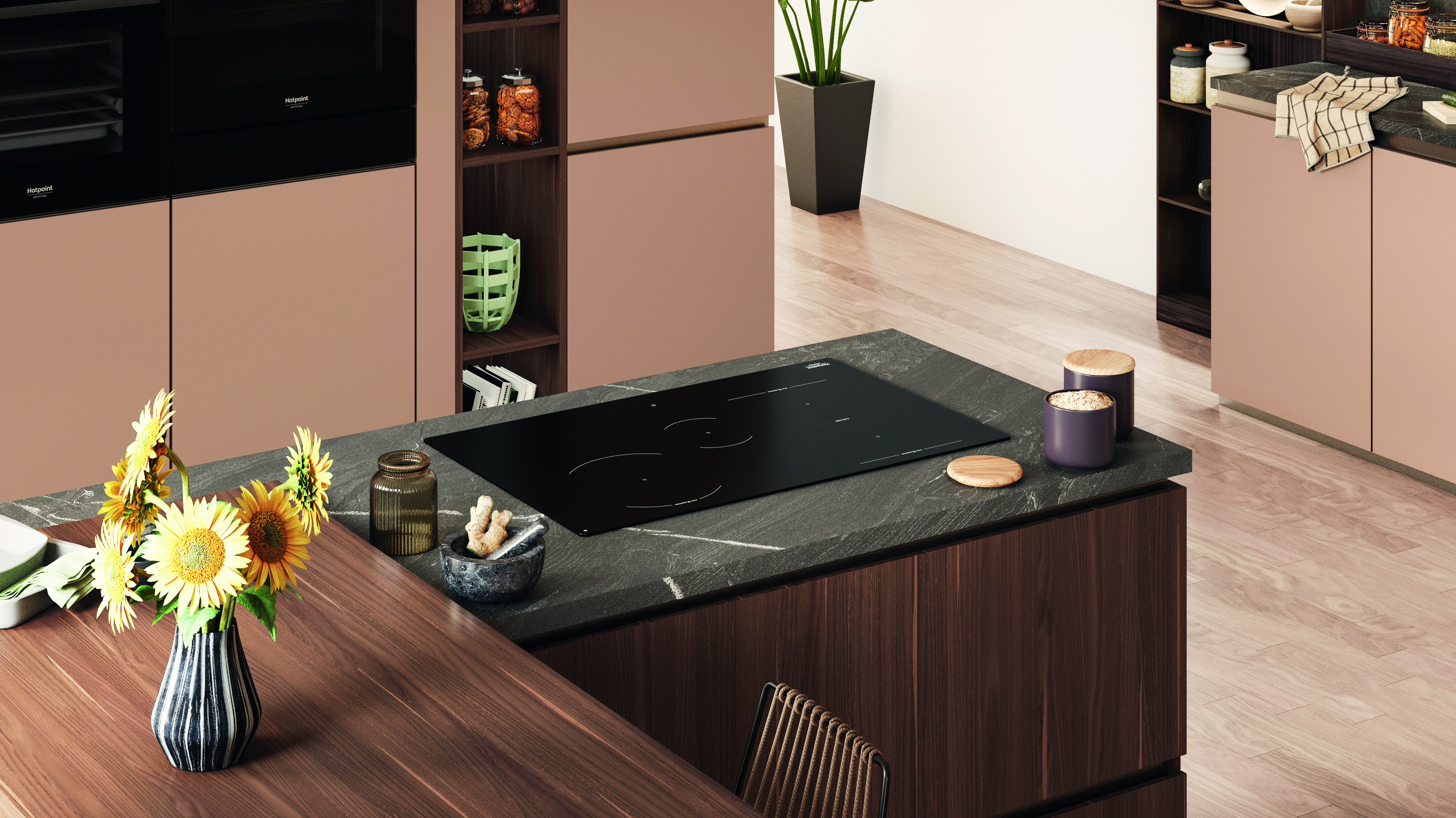 Interni cucina con piano cottura nero su un piano scuro. Girasoli in un vaso a righe. Armadi e pavimenti in legno.