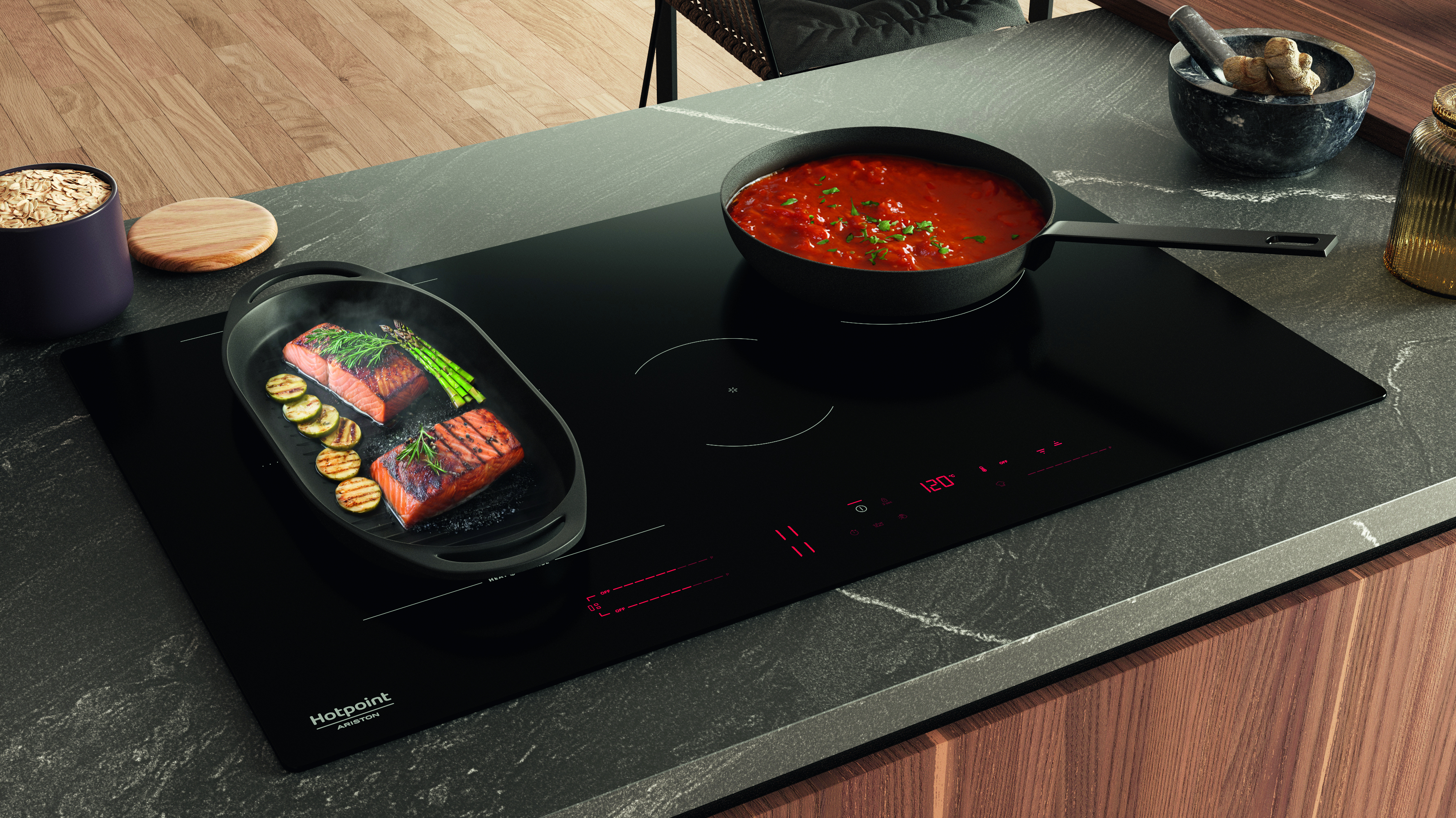 Scena di cucina con piano cottura nero, salmone, salsa in padella e ingredienti sul piano. Armadi in legno sullo sfondo.