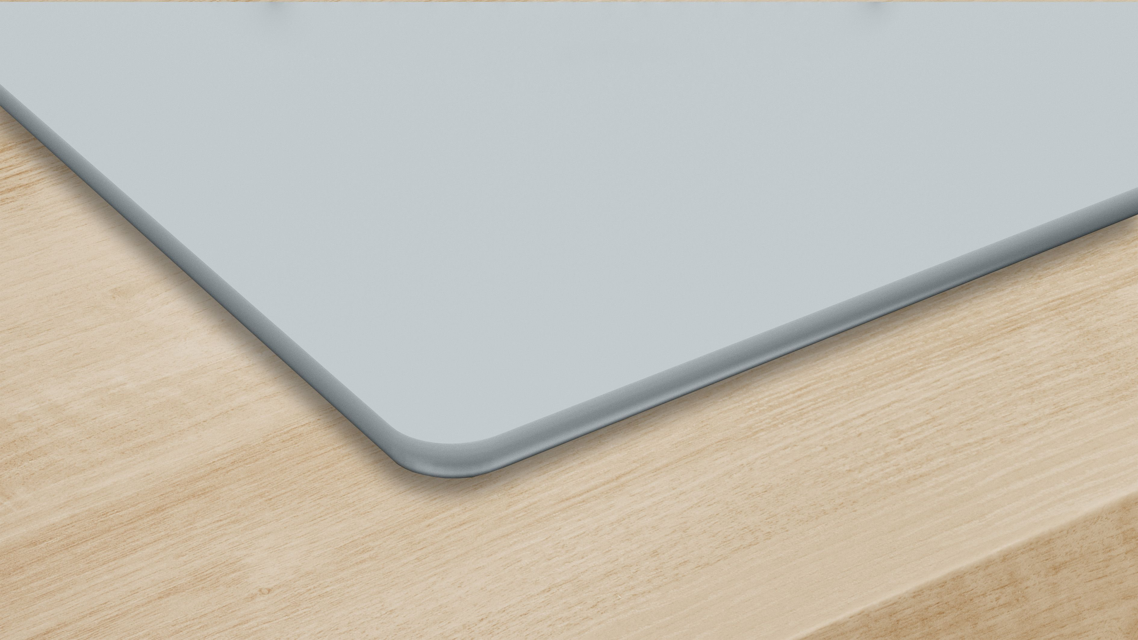 Jasnoniebieska powierzchnia z zaokrąglonym rogiem leży na jasnobrązowej drewnianej powierzchni. Powierzchnie stykają się pod kątem.