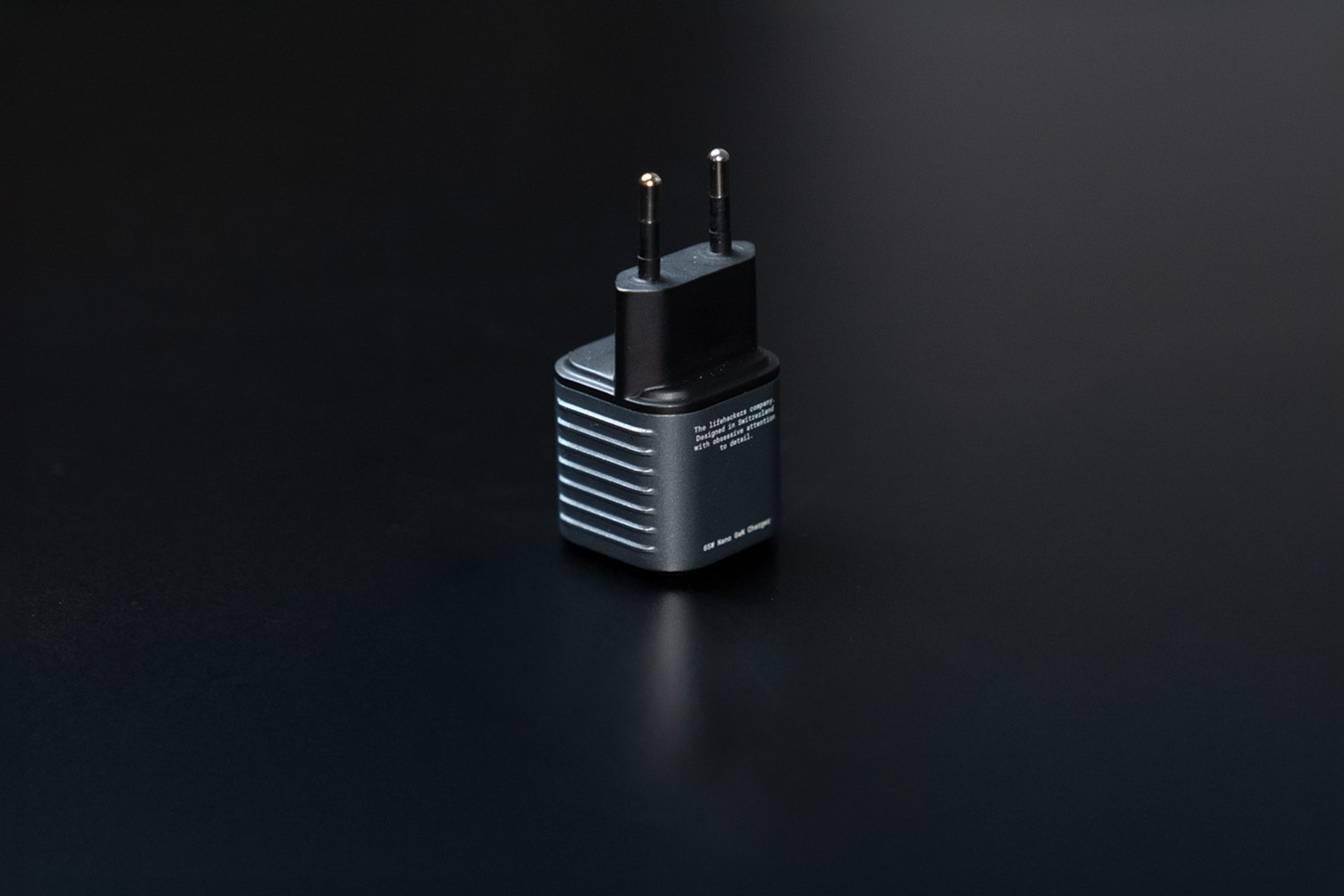 A gray and black electrical adapter on a black surface. It has two prongs and a body with text.