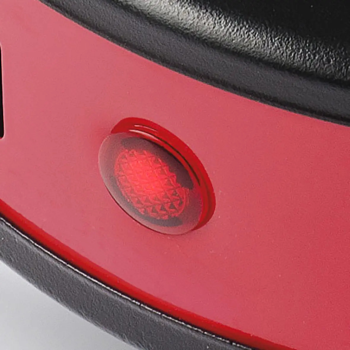 Zbliżenie czerwonego urządzenia. Wyróżnia się czerwony, podświetlony przycisk o teksturowanej powierzchni. Czarne wykończenie obramowuje czerwoną powierzchnię.