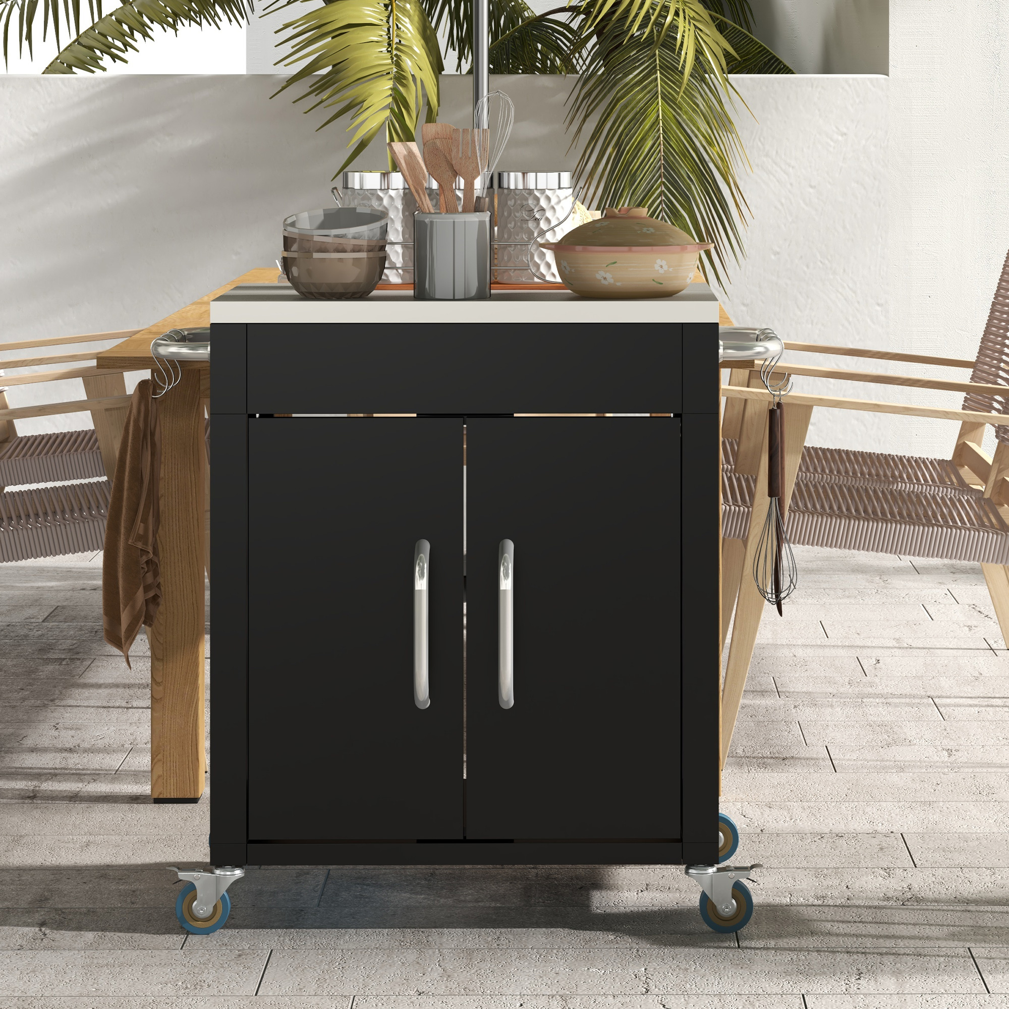 Carrello da cucina nero per esterni con maniglie e ruote in acciaio inossidabile, sotto un tavolo di legno, con utensili da cucina sopra.