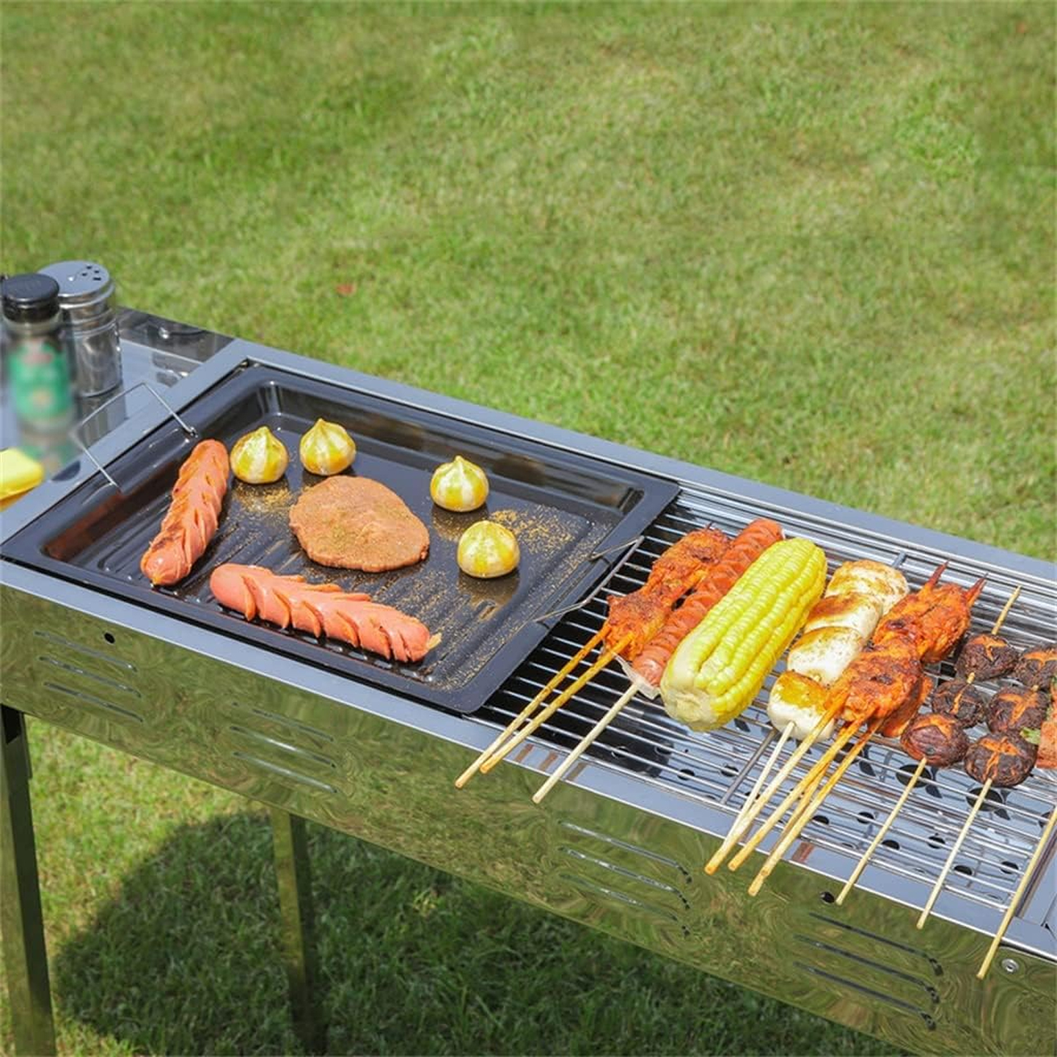 Una griglia per barbecue con vari cibi come salsicce, mais e spiedini. La griglia è su una superficie erbosa. I condimenti sono visibili.