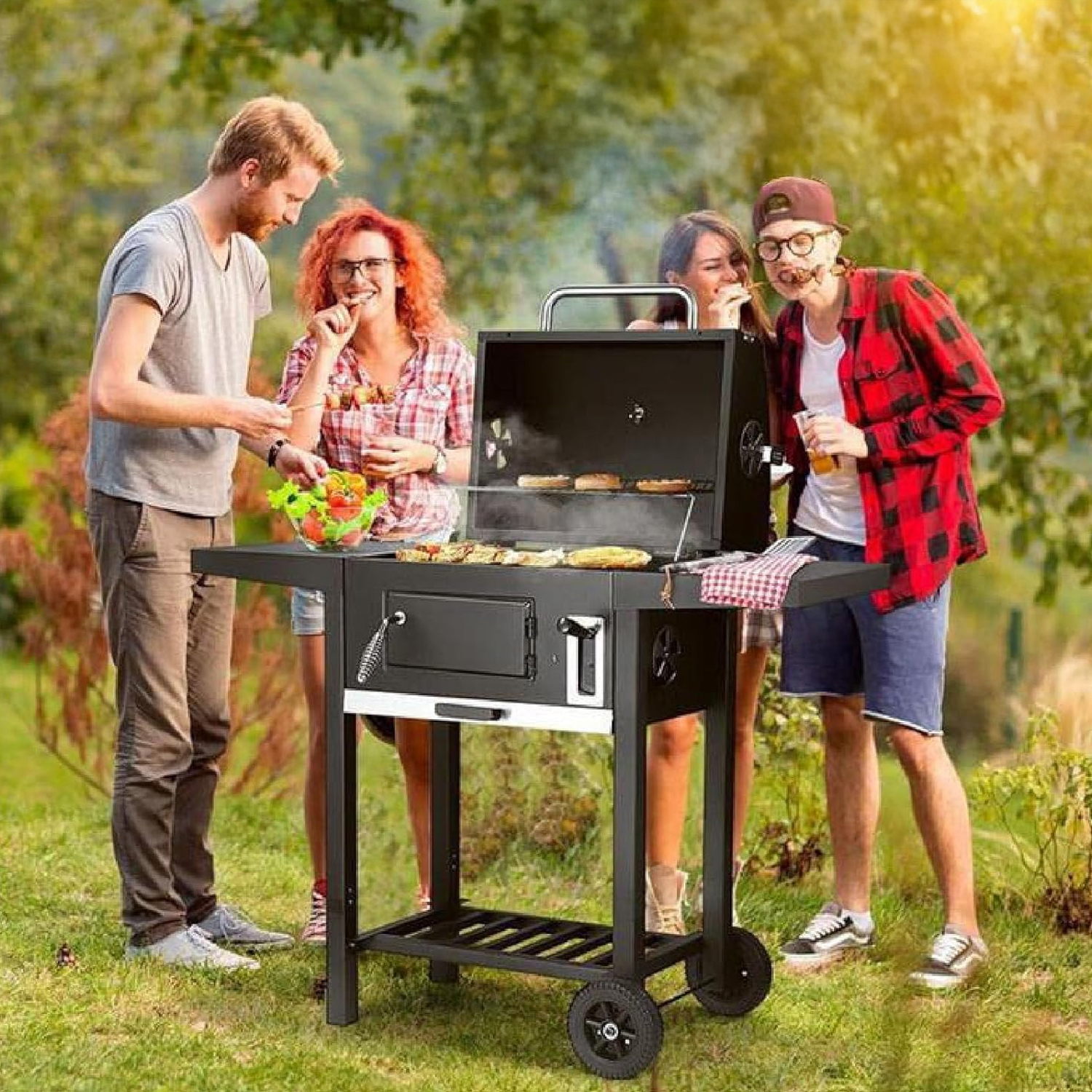 Vier Personen stehen im Freien an einem schwarzen Grill. Sie grillen Essen und lächeln. Im Hintergrund sind grüne Bäume und Gras.