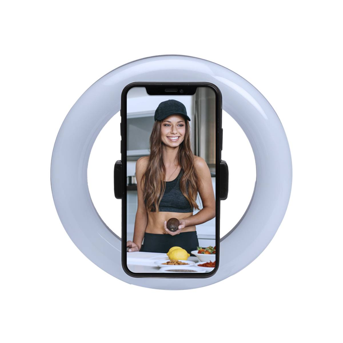 Femme en casquette et soutien-gorge de sport tenant un avocat, dans un téléphone tenu par la lumière. Nourriture sur la table.