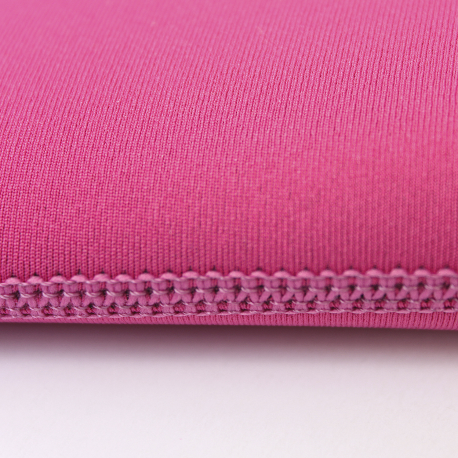 Primo piano di tessuto rosa con trama visibile e cuciture sul bordo, su una superficie bianca.