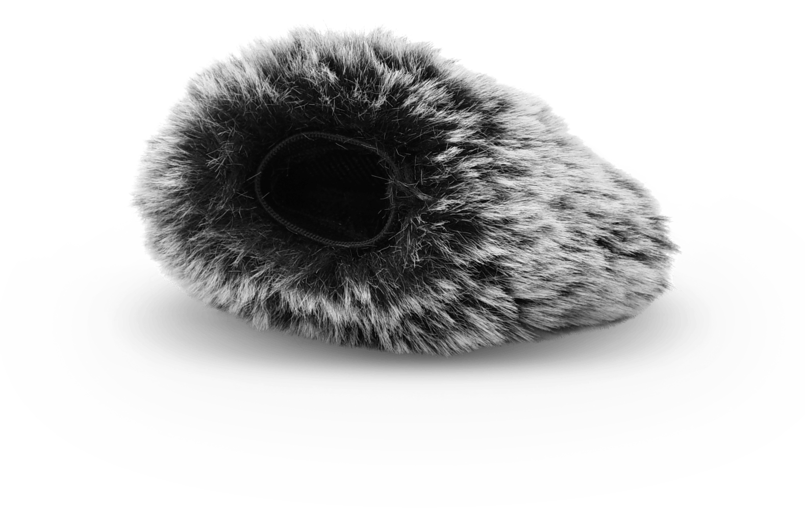 Puszysta, futrzana osłona mikrofonu, szara i czarna, leży na białej powierzchni. Ma centralny otwór i cień pod spodem.