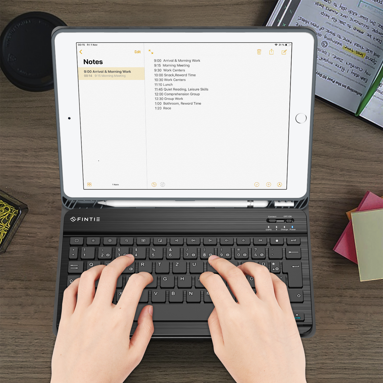 Ein iPad mit Tastatur liegt auf einem Holztisch. Der Bildschirm zeigt einen Zeitplan mit einem Stift. Hände tippen auf der Tastatur.
