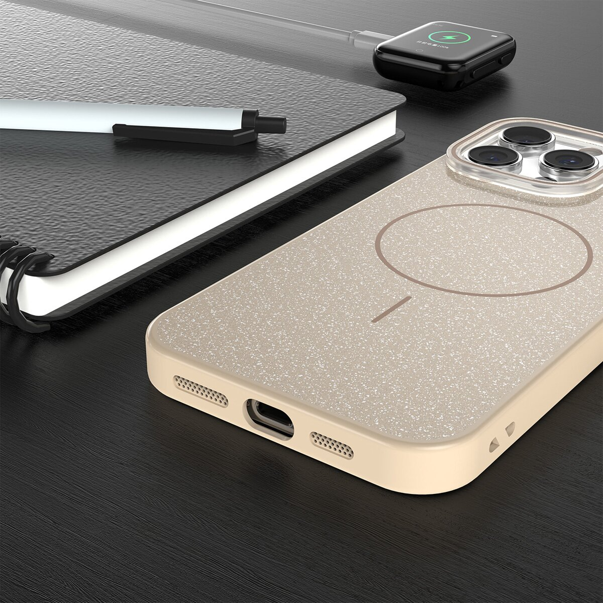 Ein Telefongehäuse, ein Notizbuch und eine ladende Apple Watch liegen auf einer dunklen Oberfläche. Das Telefongehäuse ist beige, die Uhr ist schwarz.