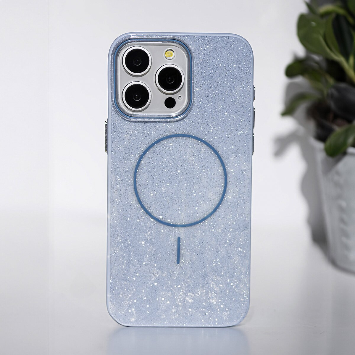Eine blaue Handyhülle mit Glitzereffekt, mit Kameramodul und kreisförmigem Design auf der Rückseite, auf weißer Oberfläche.