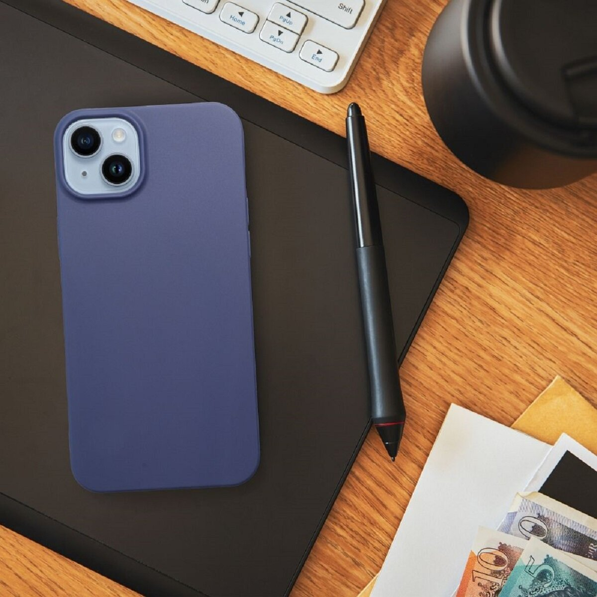 Ein blaues Telefon liegt auf einer schwarzen Oberfläche. Ein Stift, eine Tastatur und Geld liegen daneben, alles auf einem Holztisch.