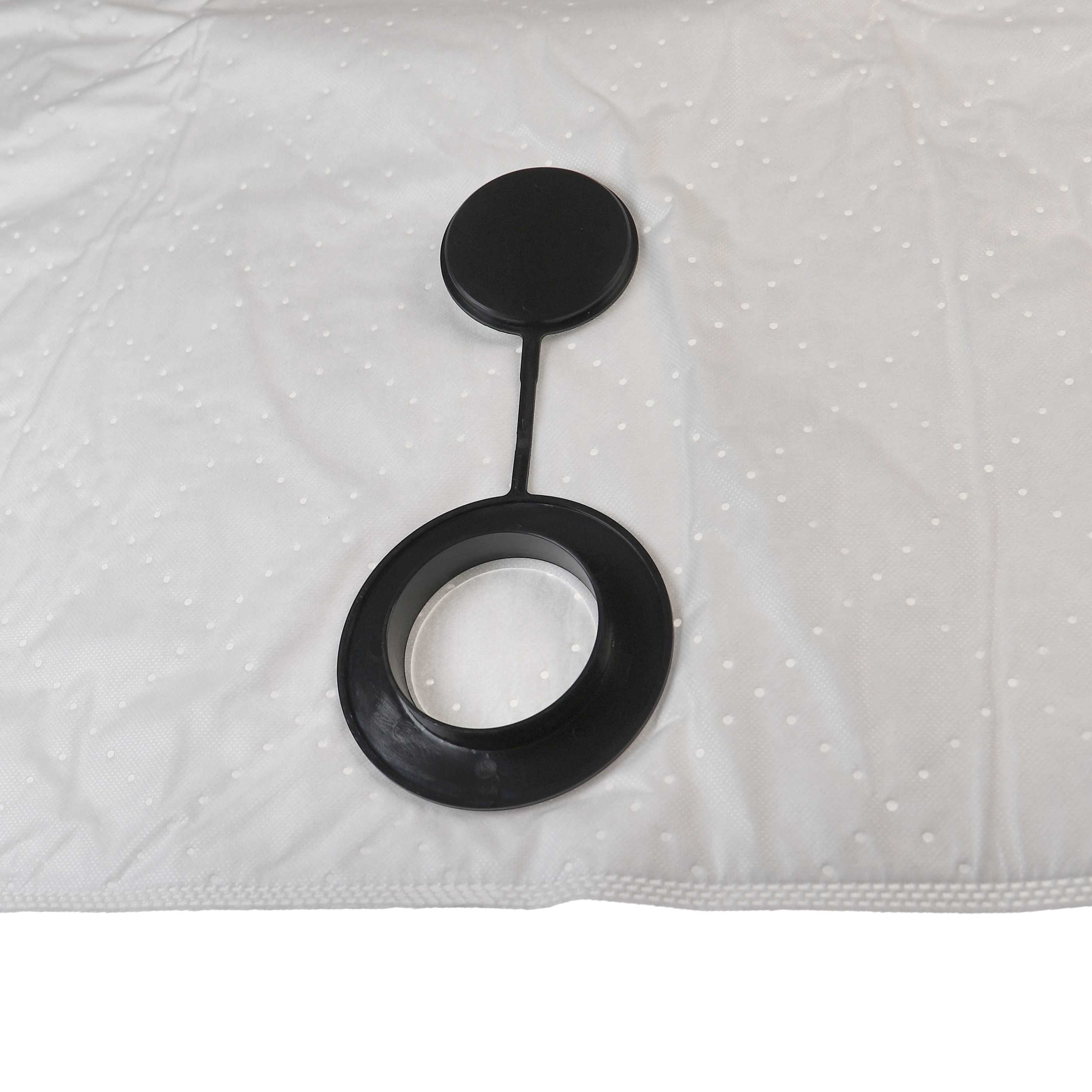 Ein schwarzes Kunststoffteil mit einer kreisförmigen Kappe, die mit einem Ring verbunden ist, liegt auf einem weißen Stoff mit Punkten.