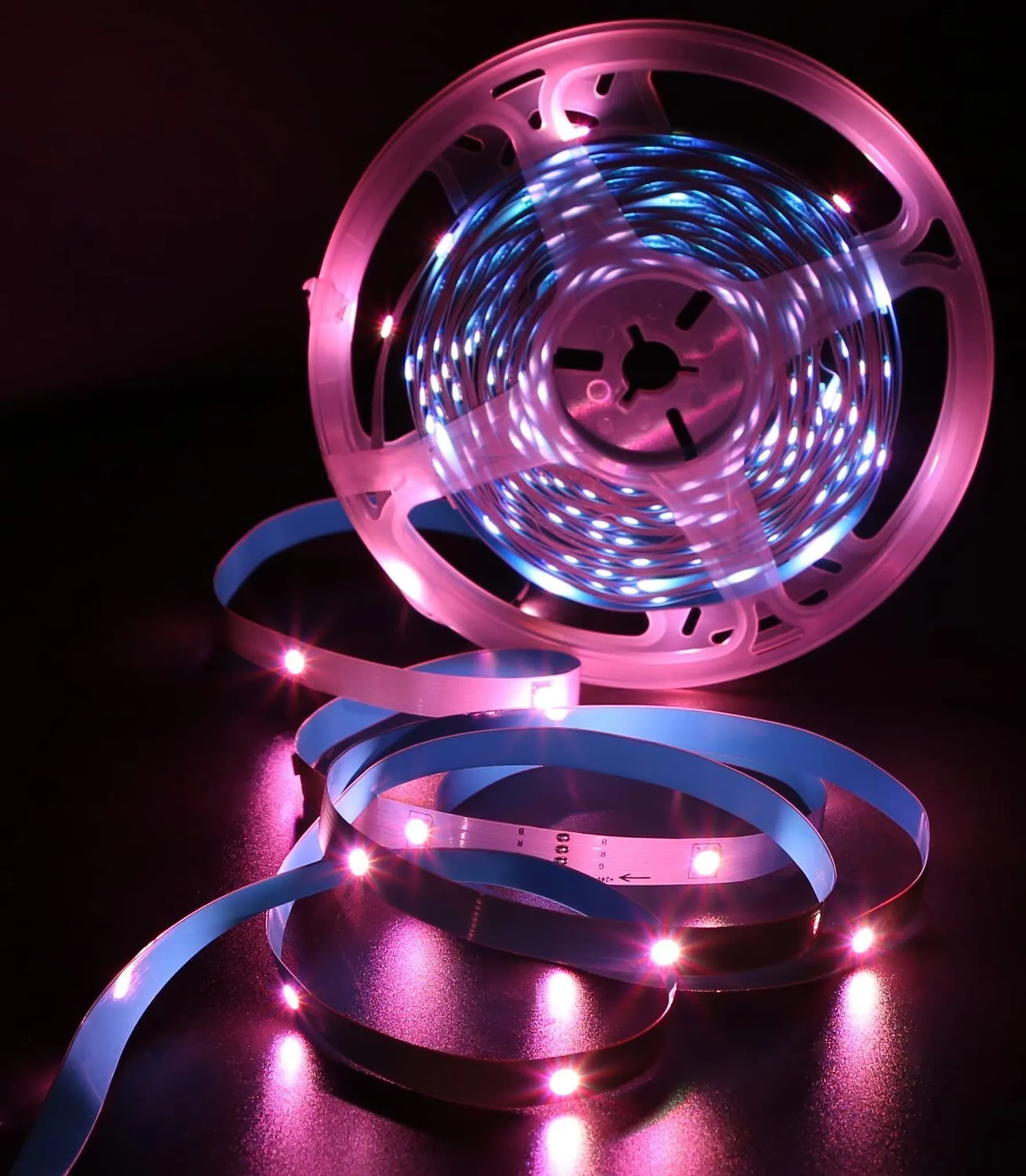 Eine Rolle LED-Streifen mit blauen und rosa Lichtern, teilweise abgerollt. Die Lichter befinden sich auf einer dunklen Oberfläche.
