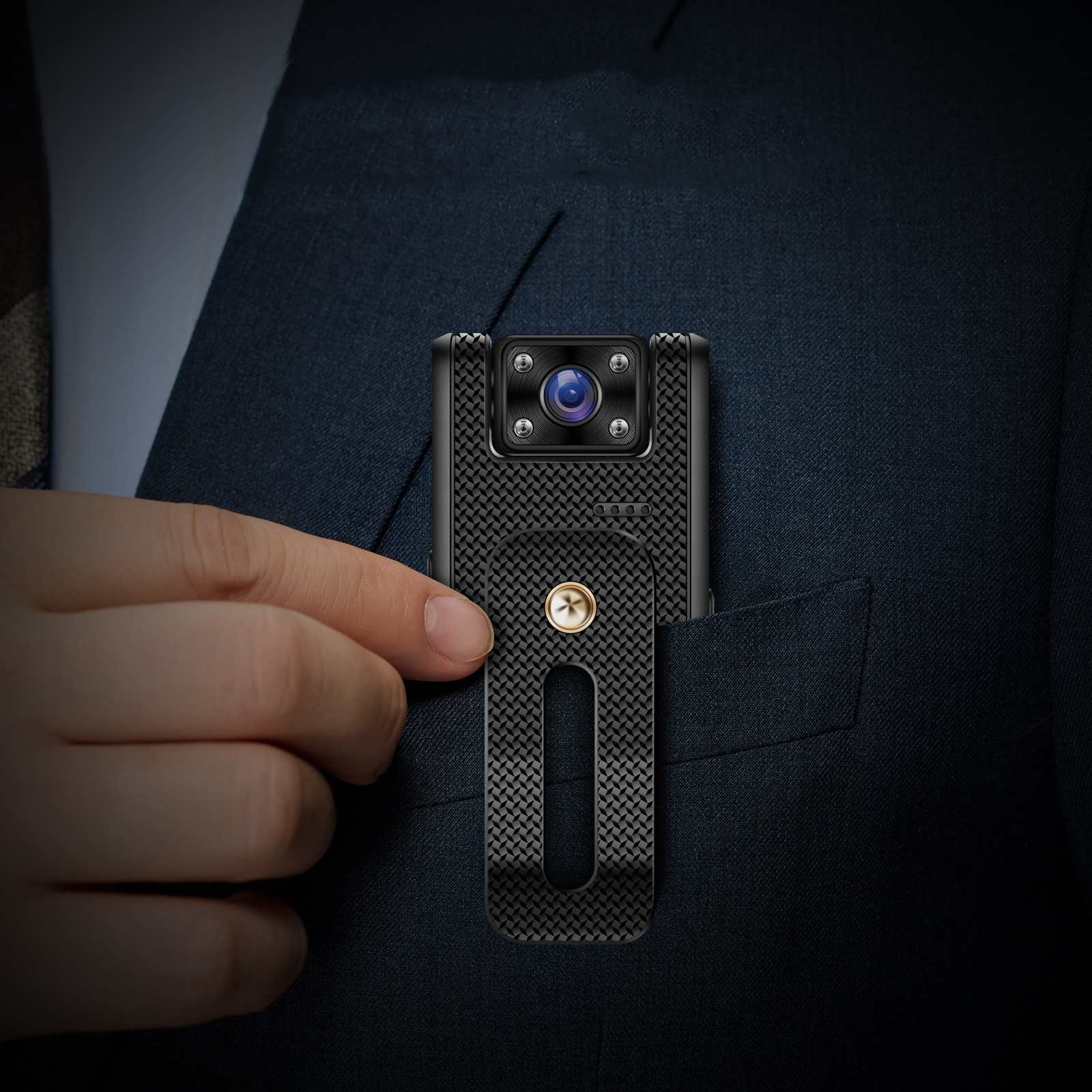 Eine kleine schwarze Kamera ist an einer Tasche befestigt. Eine Hand hält die Kamera. Der Hintergrund ist ein dunkler Anzug.