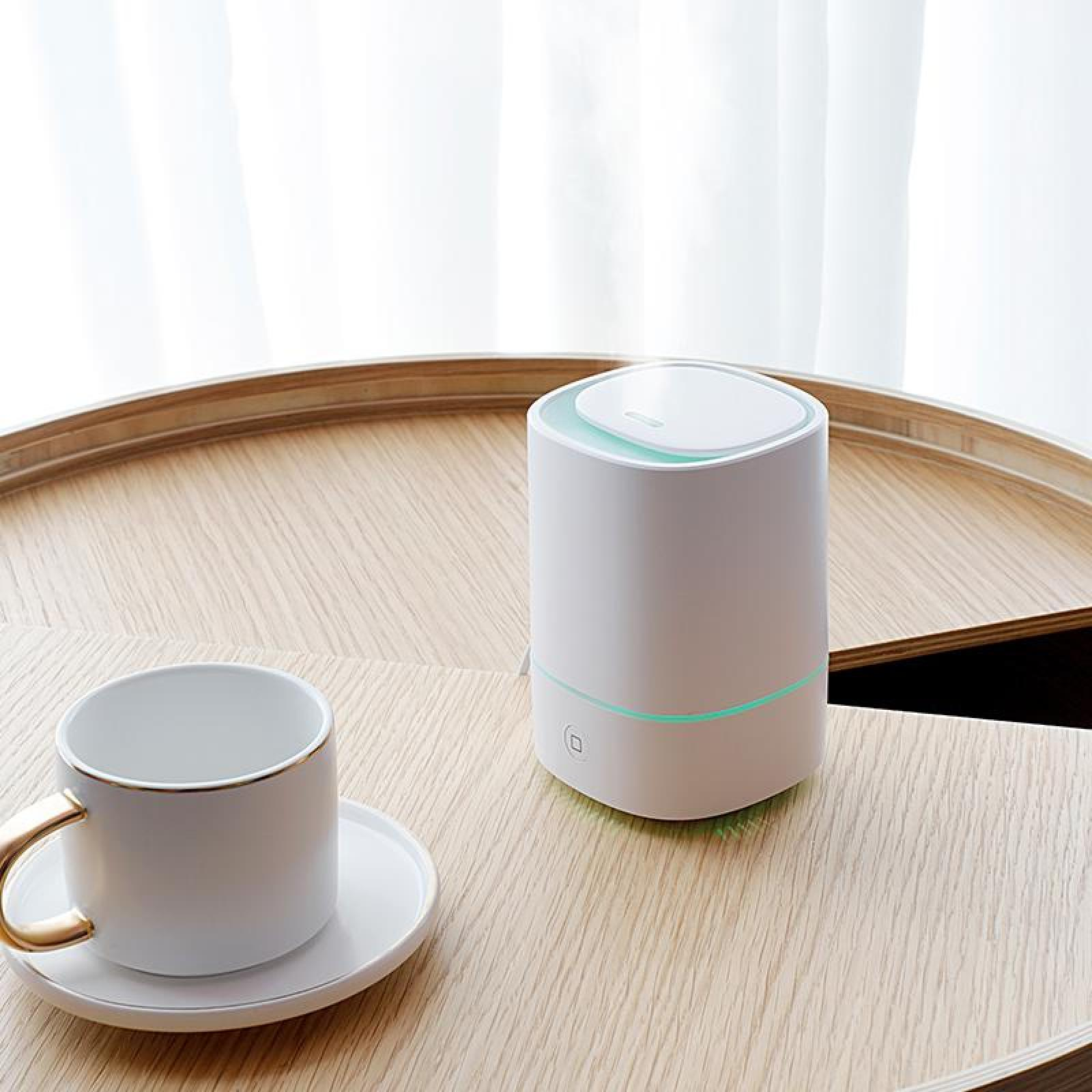 Ein weißer Luftreiniger und eine Tasse mit goldenem Griff auf einem Holztablett. Weiße Vorhänge sind im Hintergrund.
