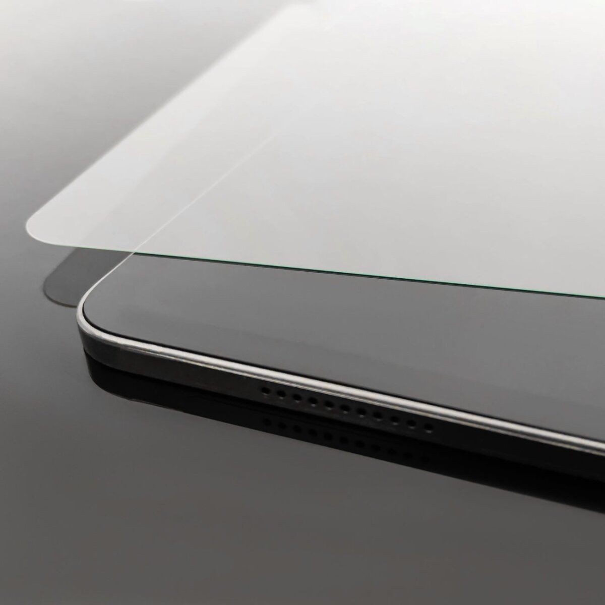 Primo piano di un tablet nero con cornice argentata e protezione schermo. La superficie è riflettente.