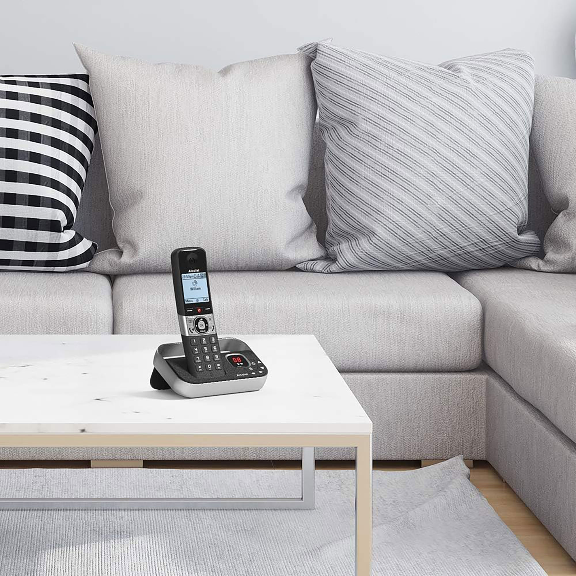 Un telefono cordless su un tavolo davanti a un divano. Cuscini sullo sfondo. La scena è ben illuminata.